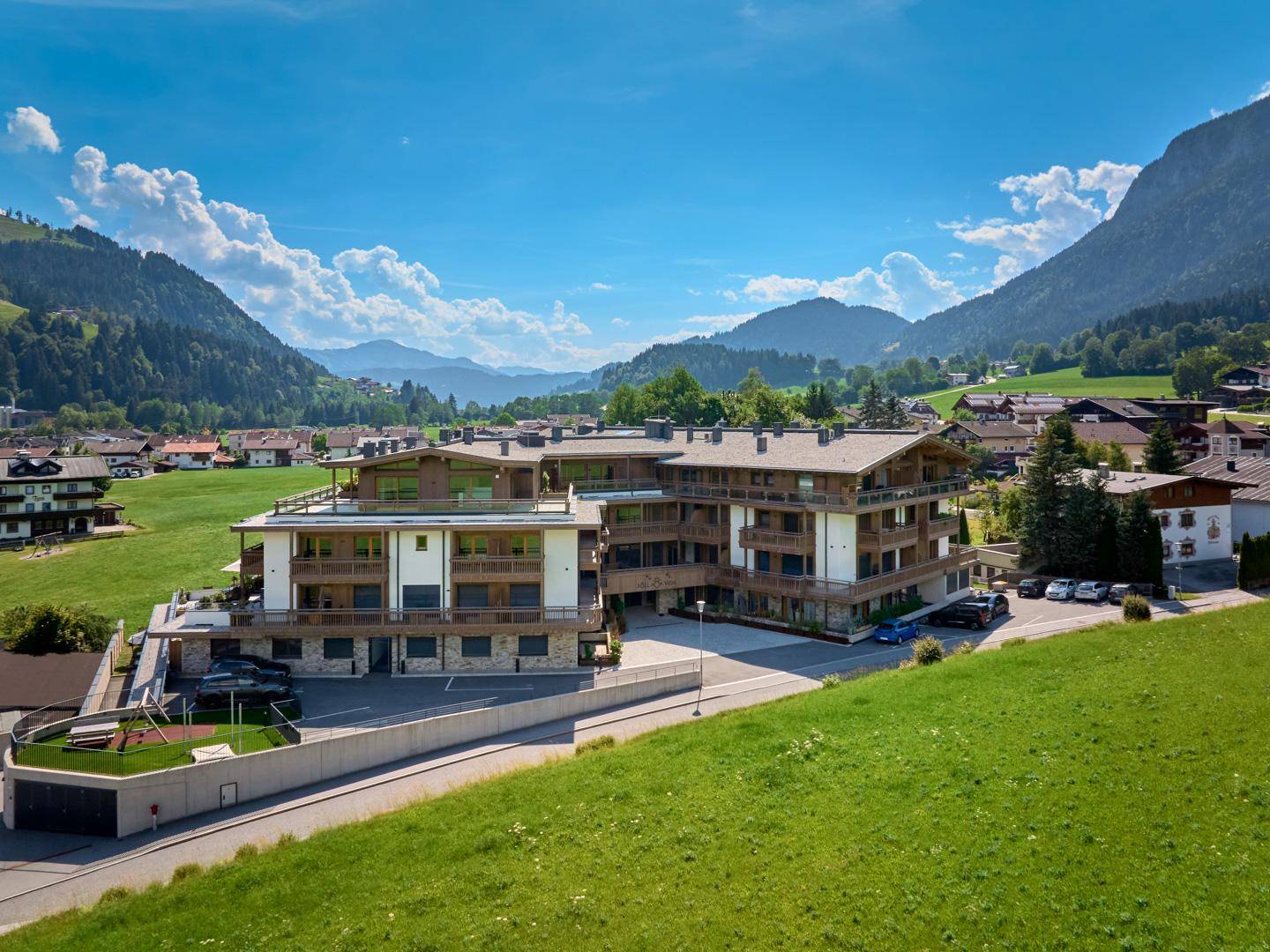 Moderne Wohnanlage in idyllischer Berglandschaft mit Spielplatz, Parkmöglichkeiten und weitem Blick auf die Berge.