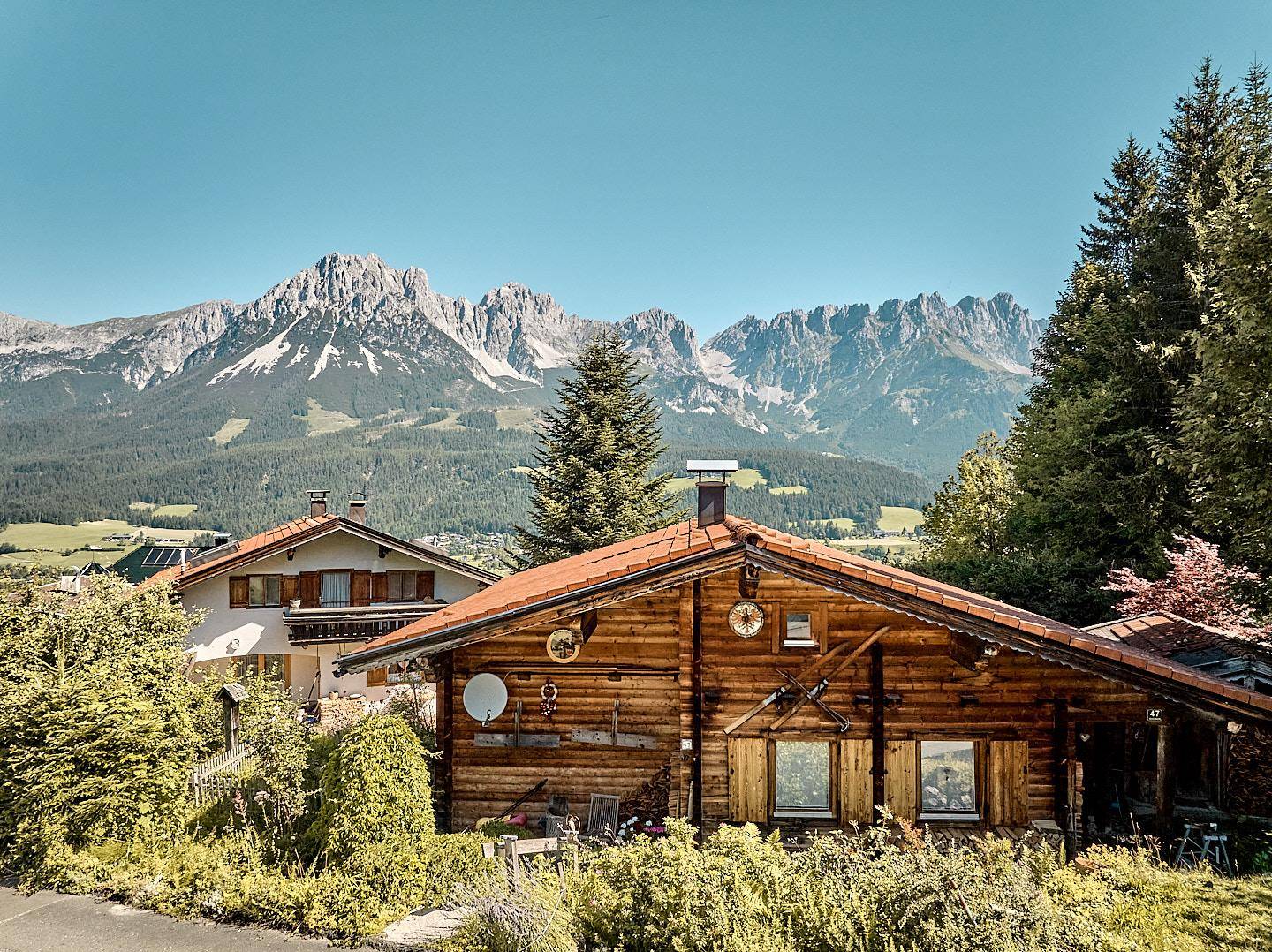 Rustikales Holzhaus mit traditioneller Architektur und beeindruckendem Bergblick unter blauem Himmel.