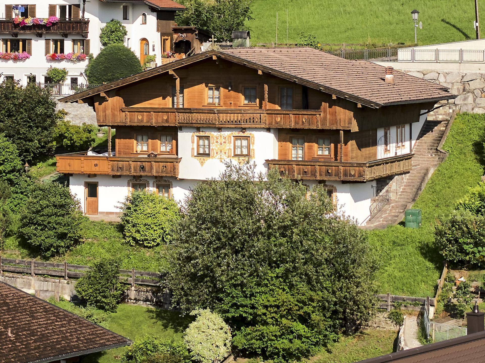 Traditionelles Holzhaus im Chalet-Stil mit mehreren Balkonen, eingebettet in eine grüne Hanglage.
