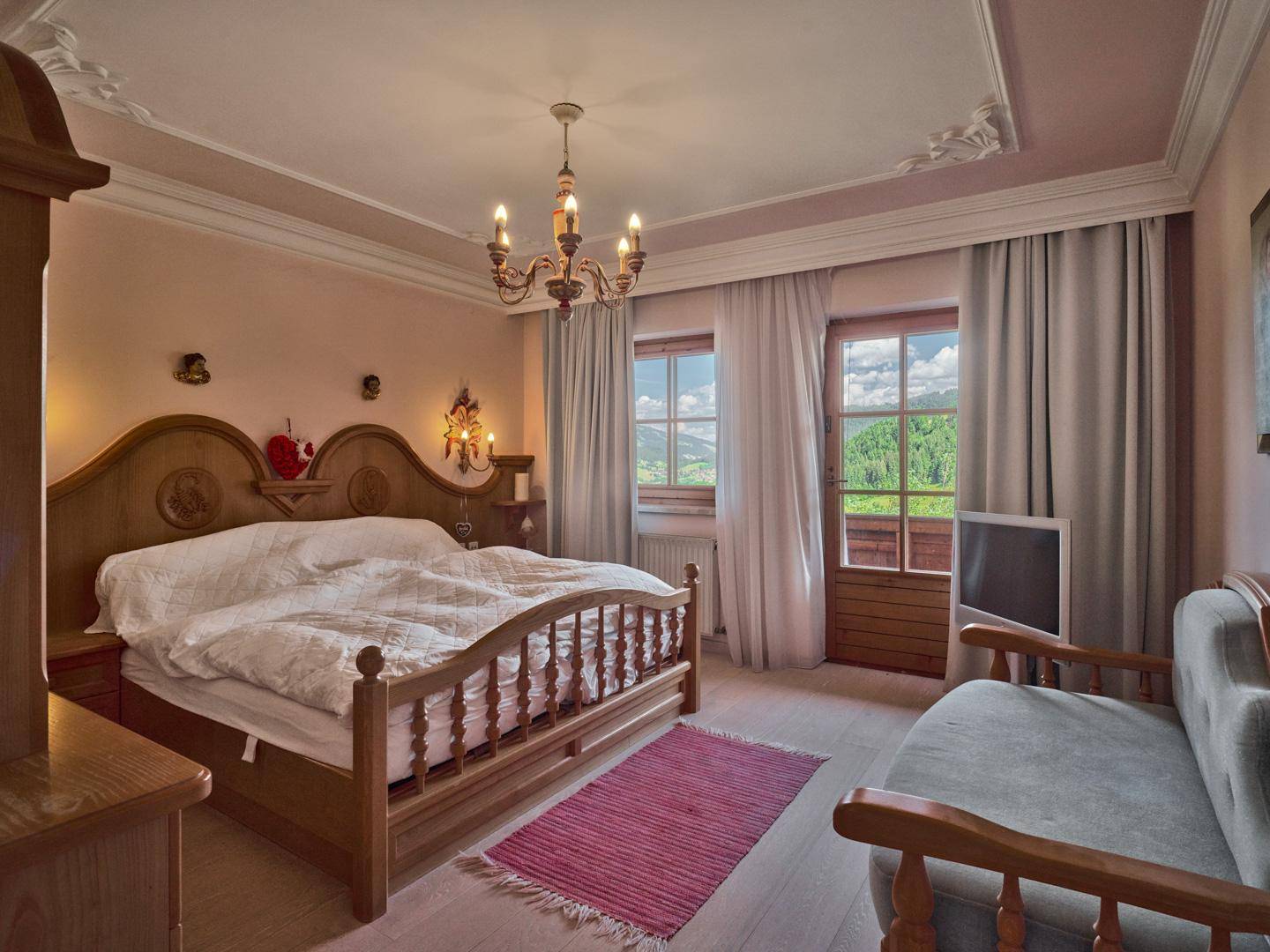 Helles Schlafzimmer mit traditionellem Holzbett, Stuckdecke und direktem Zugang zu einem Balkon mit Bergblick.