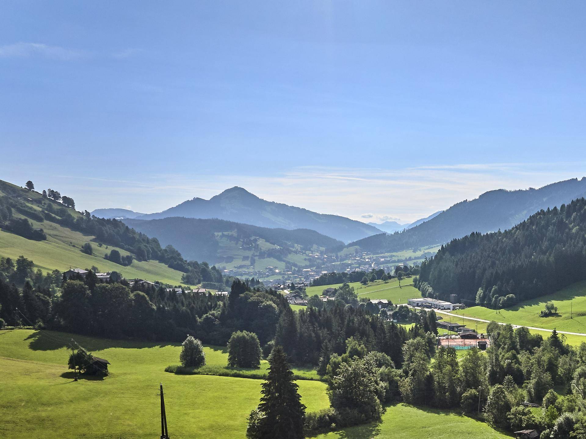 Malerischer Panoramablick über ein grünes Tal mit Bergen und einem charmanten Dorf unter blauem Himmel.
