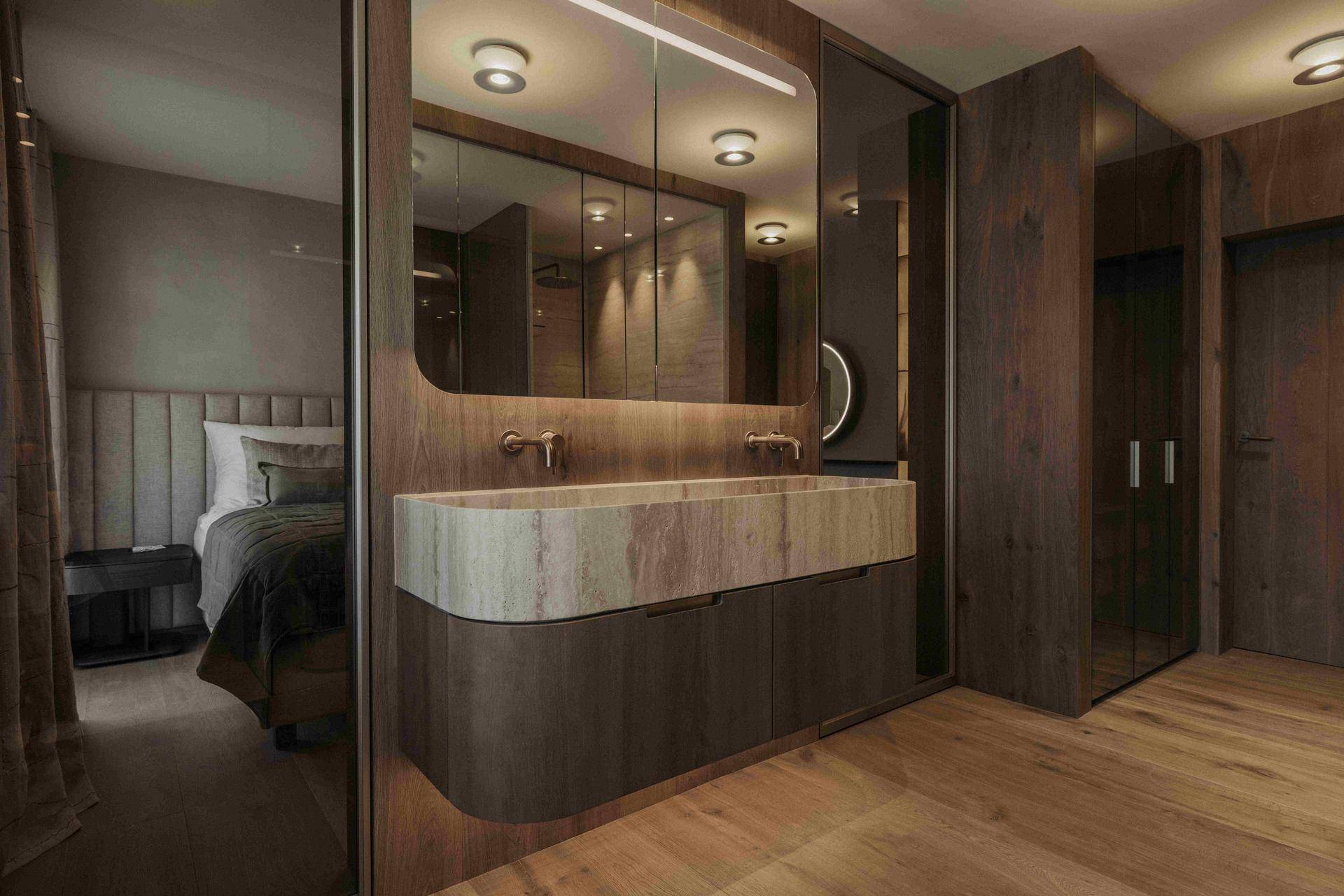 Luxuriöses Badezimmer mit Doppelwaschbecken aus Naturstein und Holzelementen, direkt am Schlafzimmer.