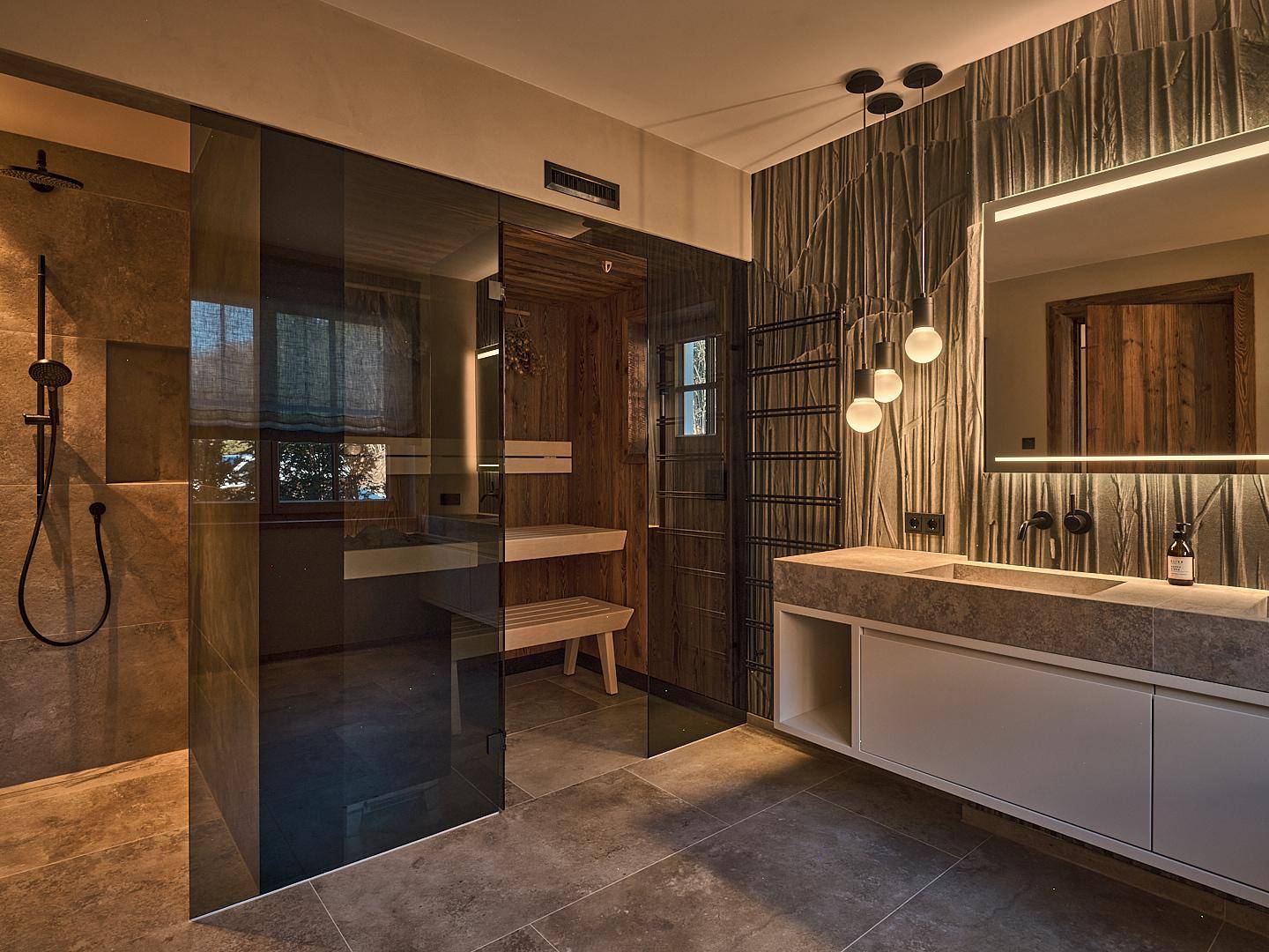 Luxuriöses Badezimmer mit begehbarer Dusche, integrierter Sauna, Doppelwaschbecken und beleuchtetem Spiegel.