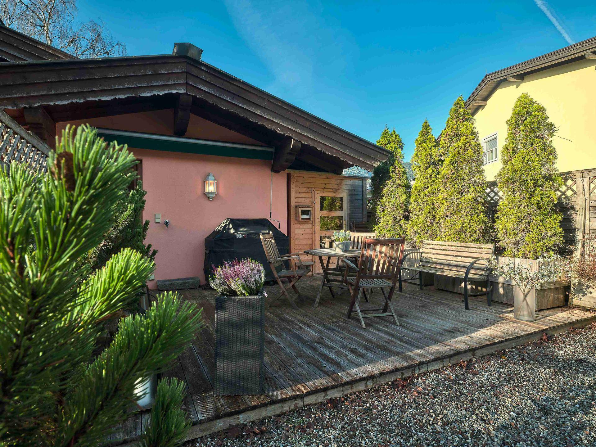 Gemütliche Holzterrasse mit Grillbereich und Gartenmöbeln vor dem Haus.
