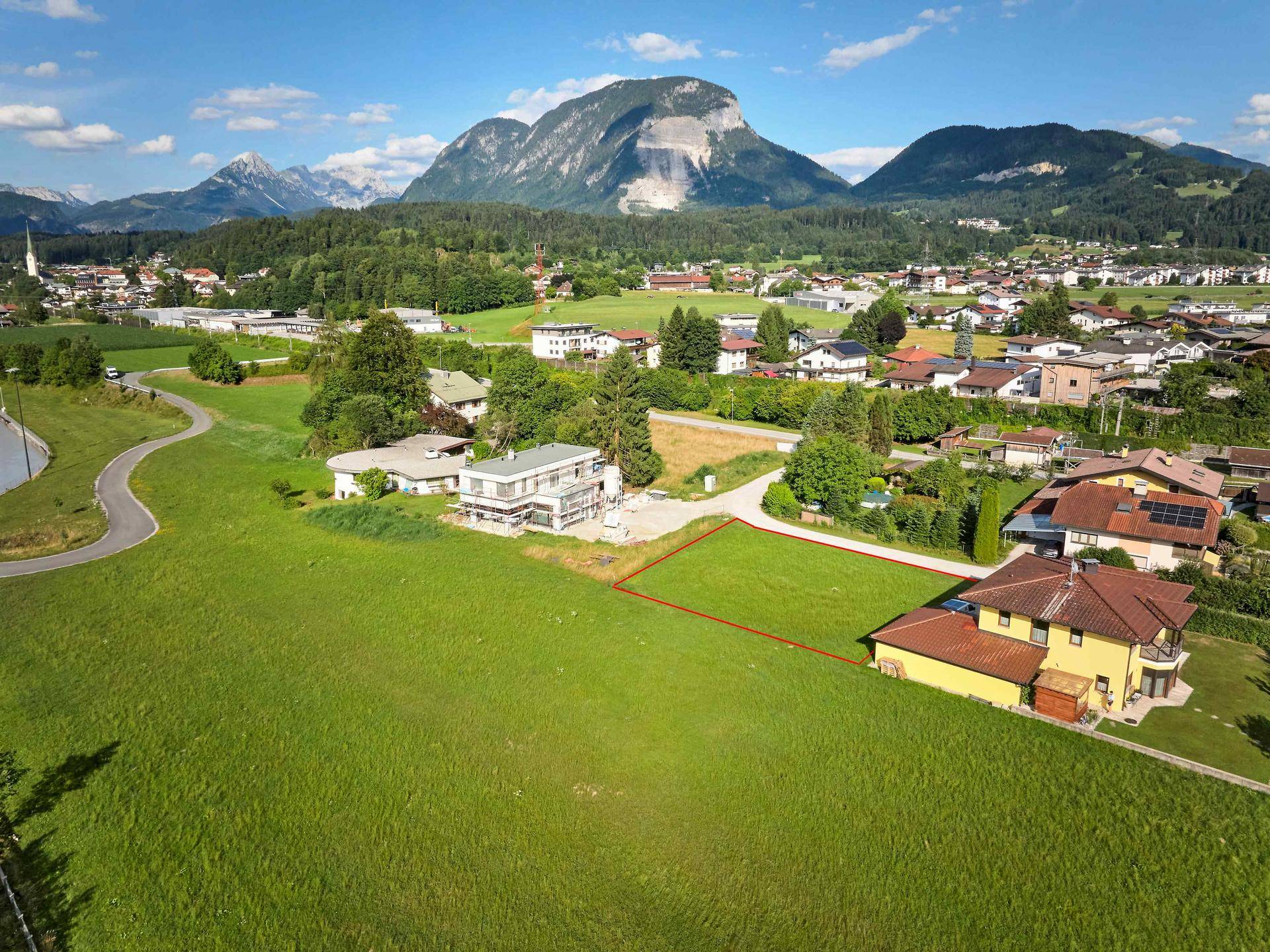 Luftaufnahme eines Baugrundstücks in einer Wohngegend mit Bergblick und Neubau in der Nähe.