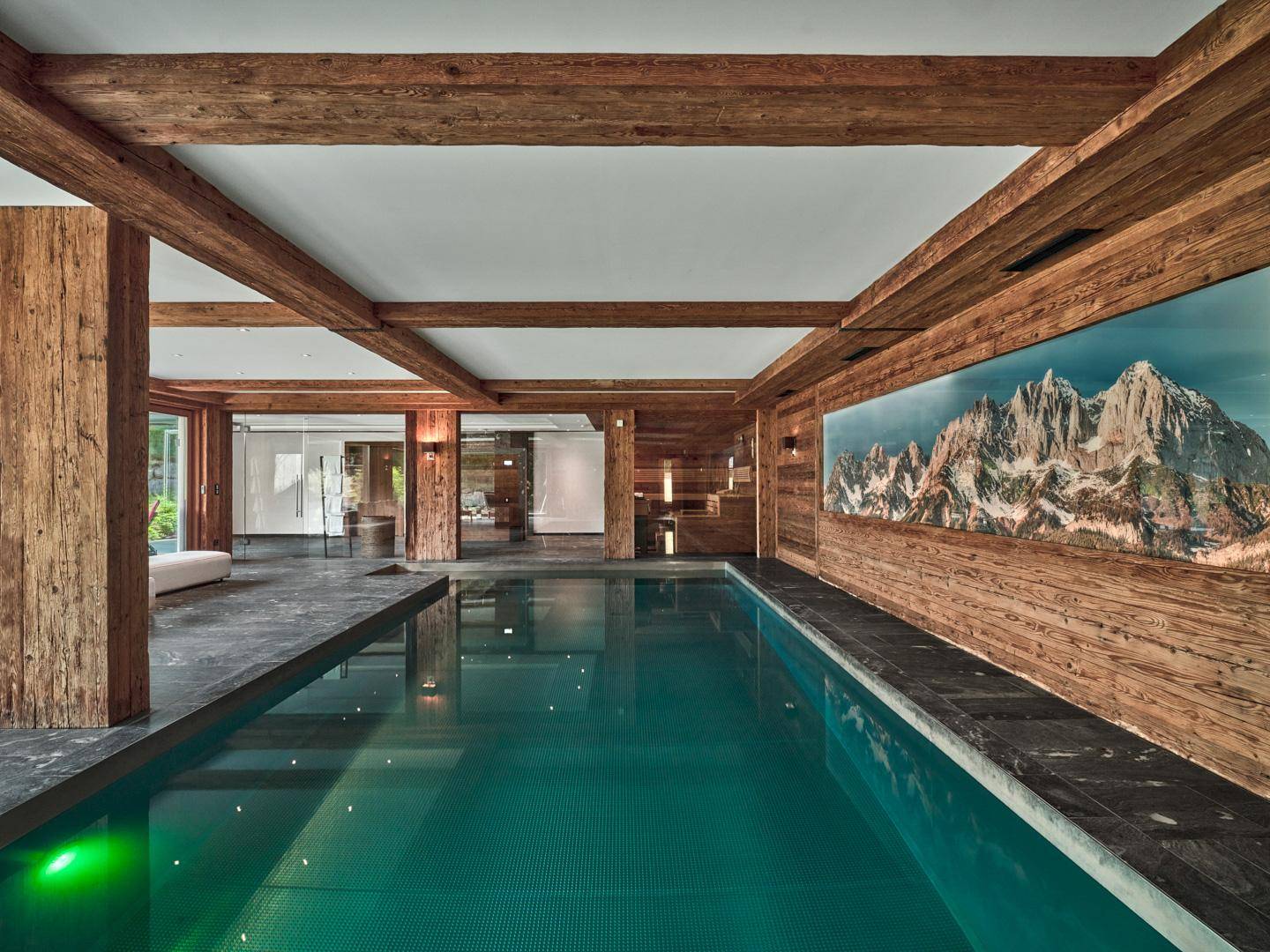 Exklusiver Innenpoolbereich mit Holzbalken, Steinboden und beeindruckendem Bergpanorama-Wandbild.