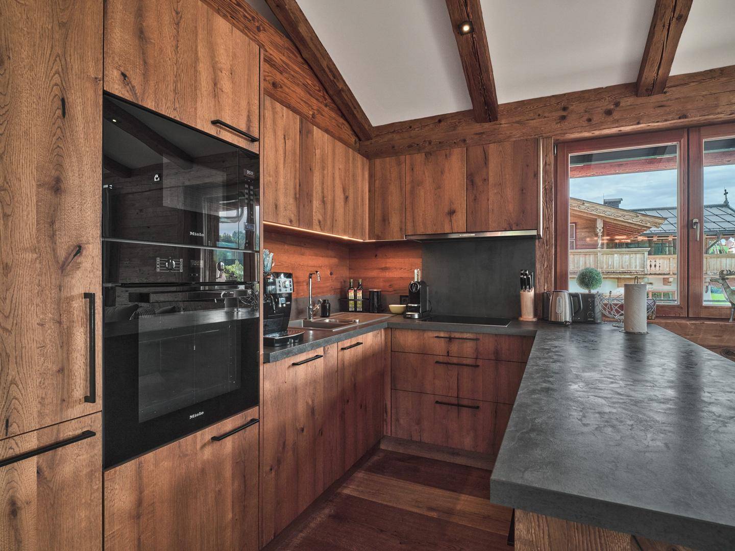 Moderne Holzküche mit hochwertigen Miele-Einbaugeräten und dunkler Arbeitsplatte.