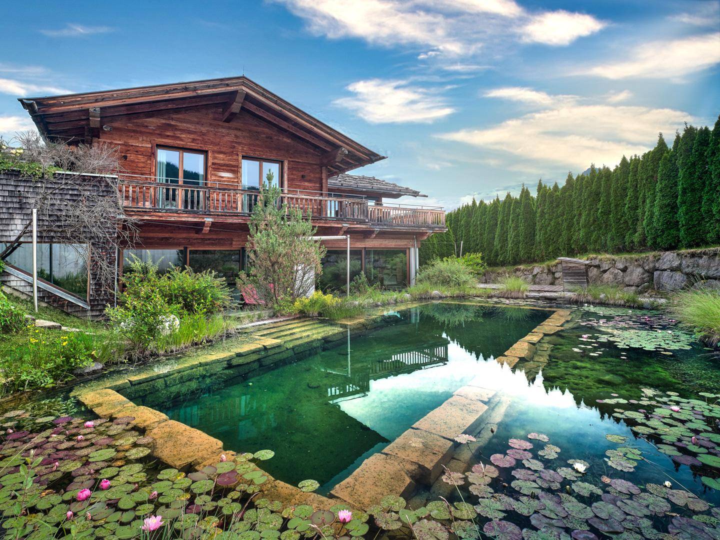 Rückseite des Chalets mit naturnahem Schwimmteich, Seerosen und üppiger Bepflanzung.