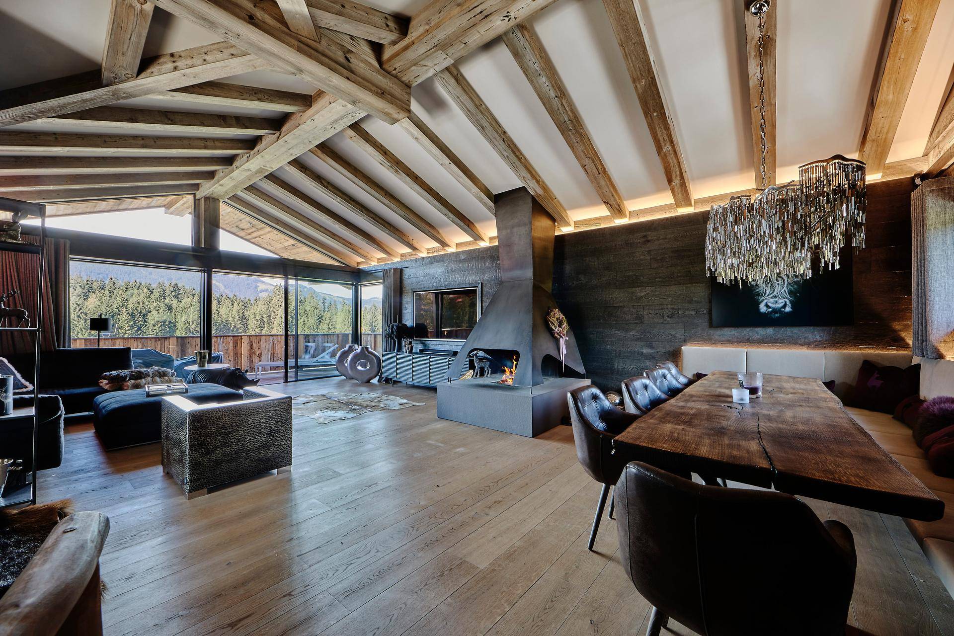 Geräumiger Wohn-Essbereich mit Holzbalkendecke, modernem Kamin und Panoramablick auf die Berge.