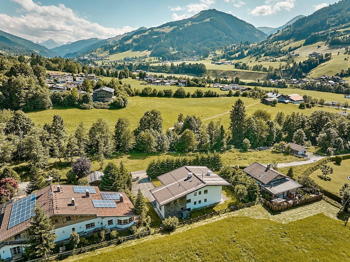 Luftaufnahme von Häusern in einer grünen Tallandschaft mit Bergen im Hintergrund.