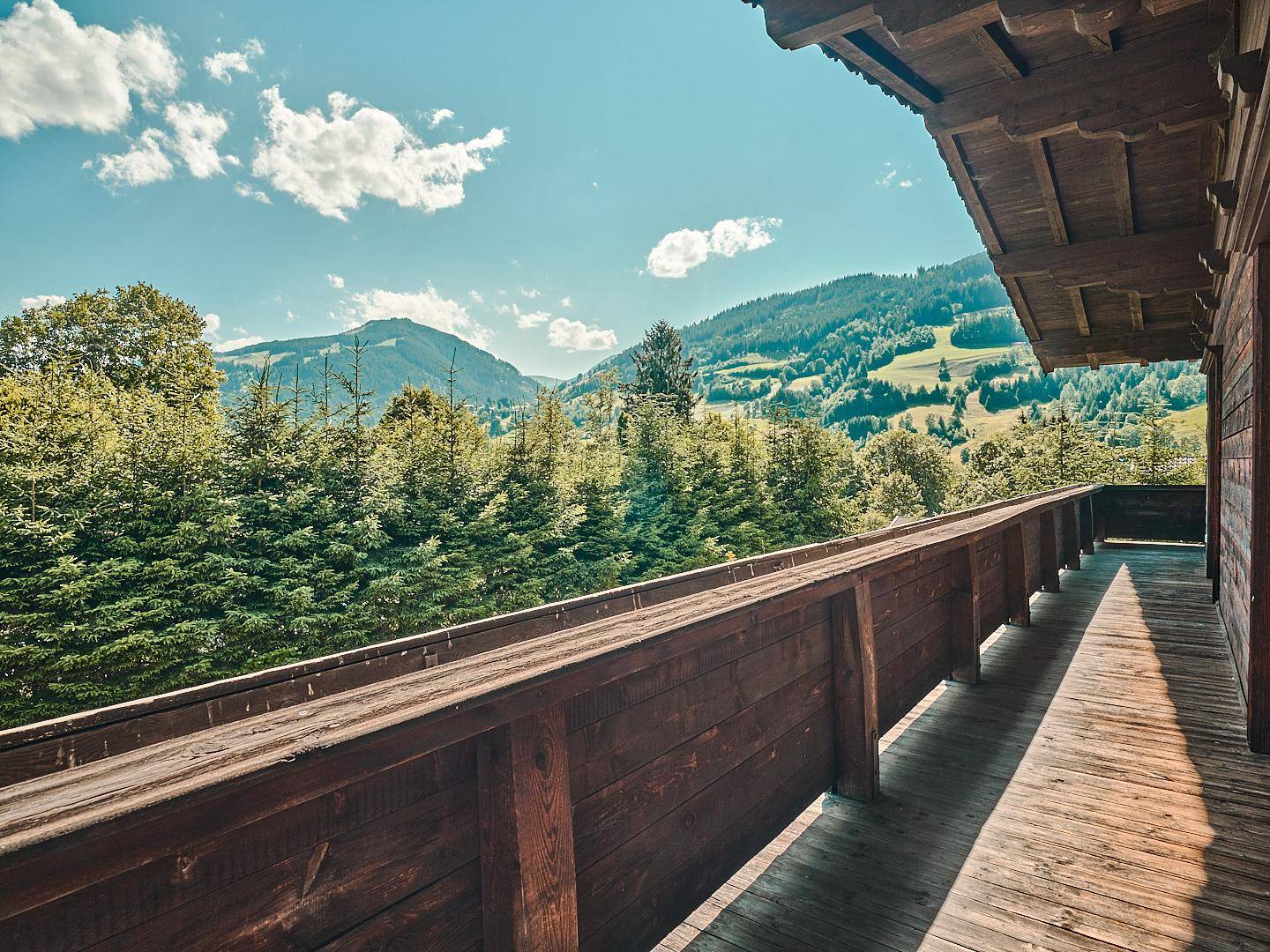 Geräumiger Holzbalkon mit Panoramablick auf die umliegende Berglandschaft und Wälder.