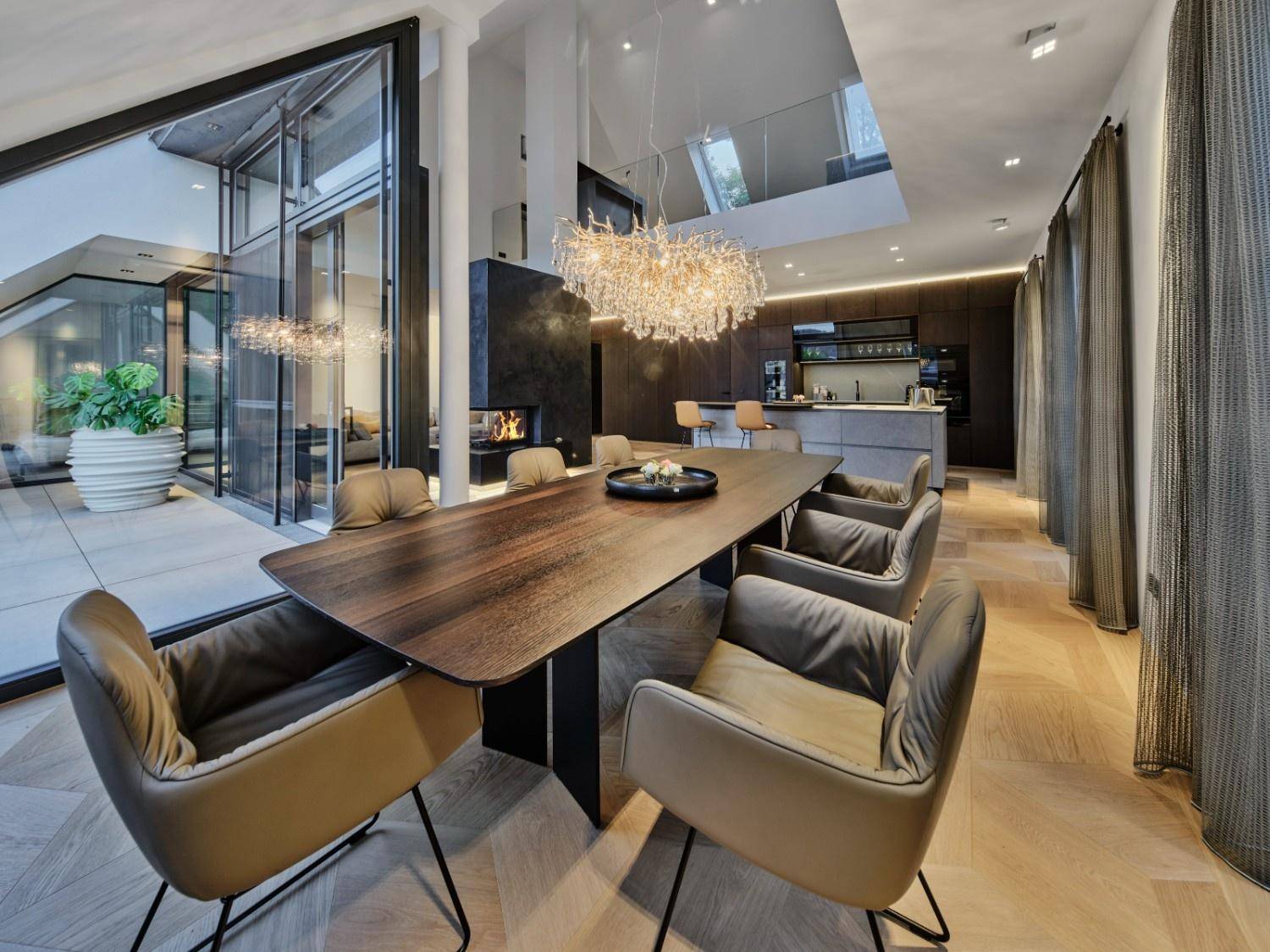 Eleganter Essbereich mit großem Holztisch, Designer-Kronleuchter und offener Küche.