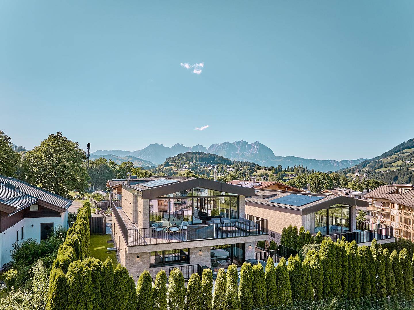 Moderne Wohnanlage mit Flachdächern, großen Glasfronten, Balkonen und Bergblick aus der Vogelperspektive.