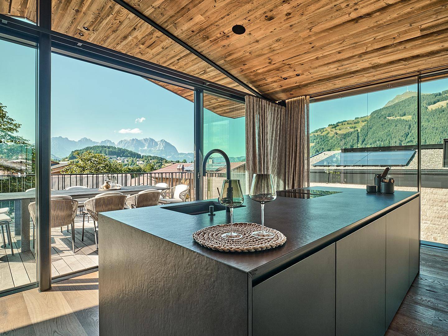 Moderne Küche mit Kochinsel, Induktionskochfeld und Zugang zu einer Terrasse mit Panoramablick auf die Berge.