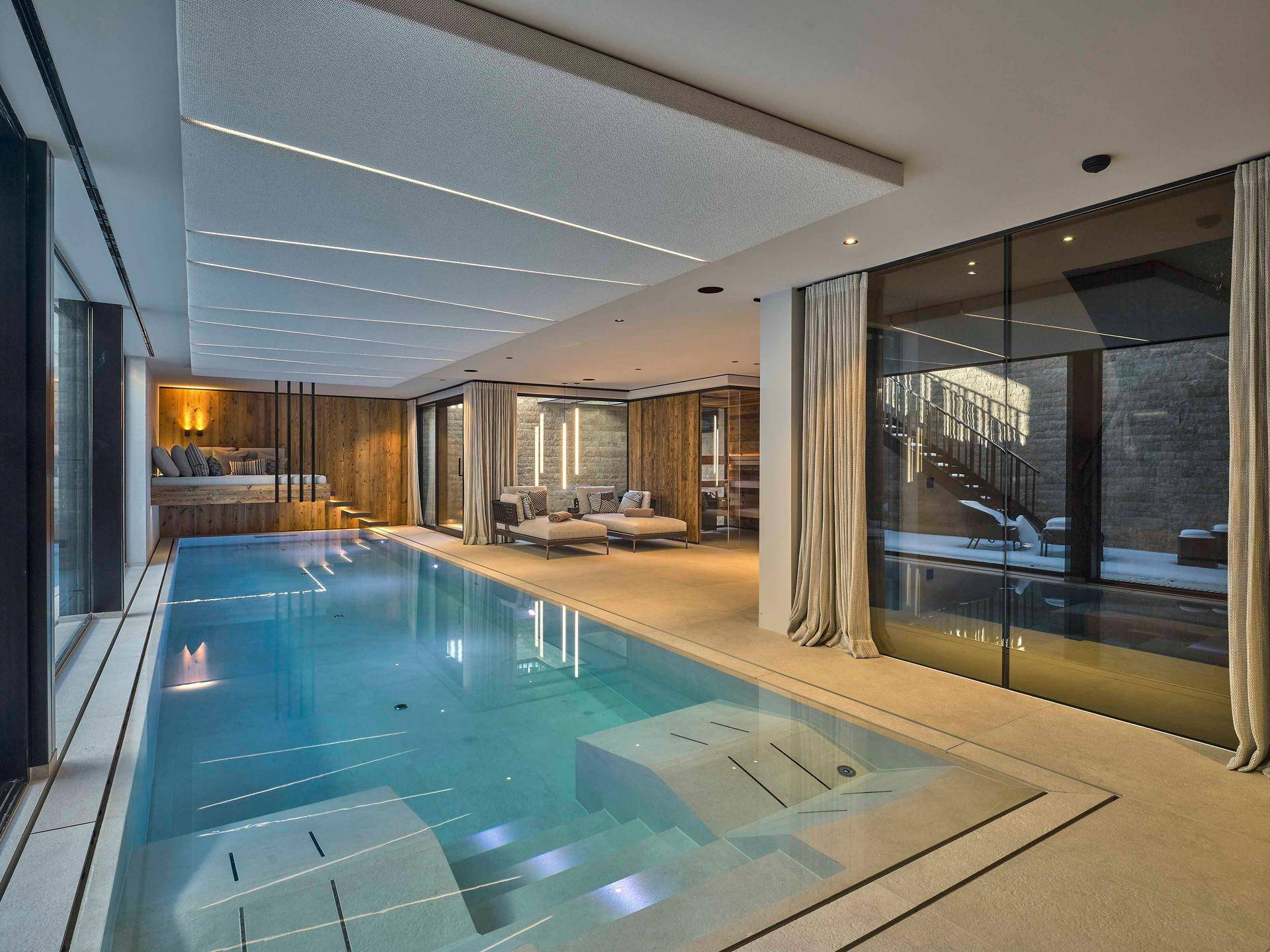 Luxuriöser Innenpoolbereich mit moderner Beleuchtung, Holzverkleidung und Entspannungsliegen.
