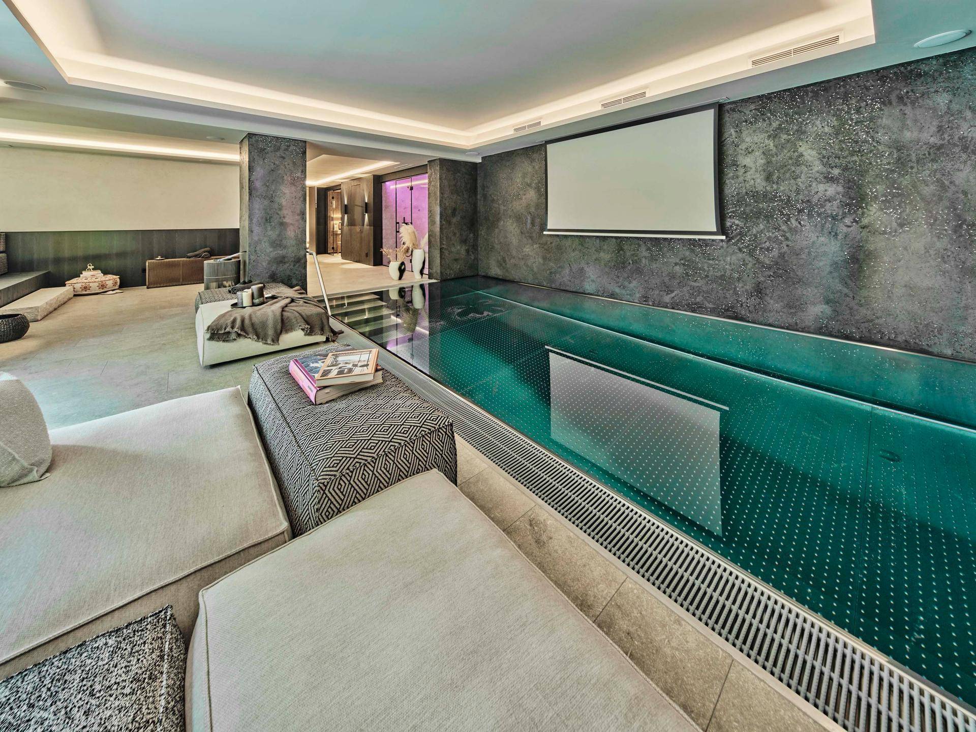 Exklusiver Wellnessbereich mit einem eleganten Innenpool, Leinwand und Entspannungszone.
