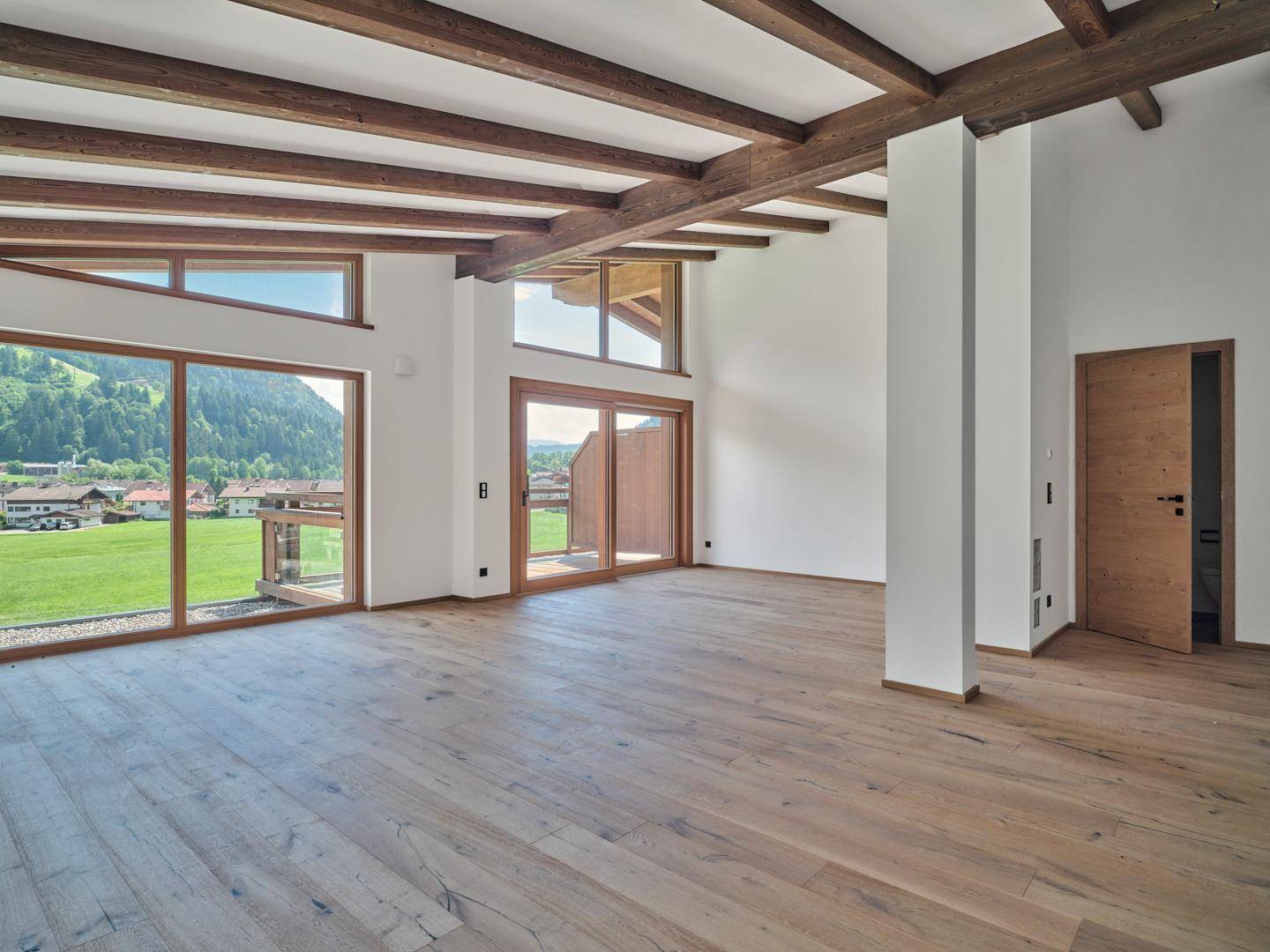 Heller Wohnbereich mit Holzbalken, Eichenparkett und Zugang zu einem Balkon mit Bergblick.