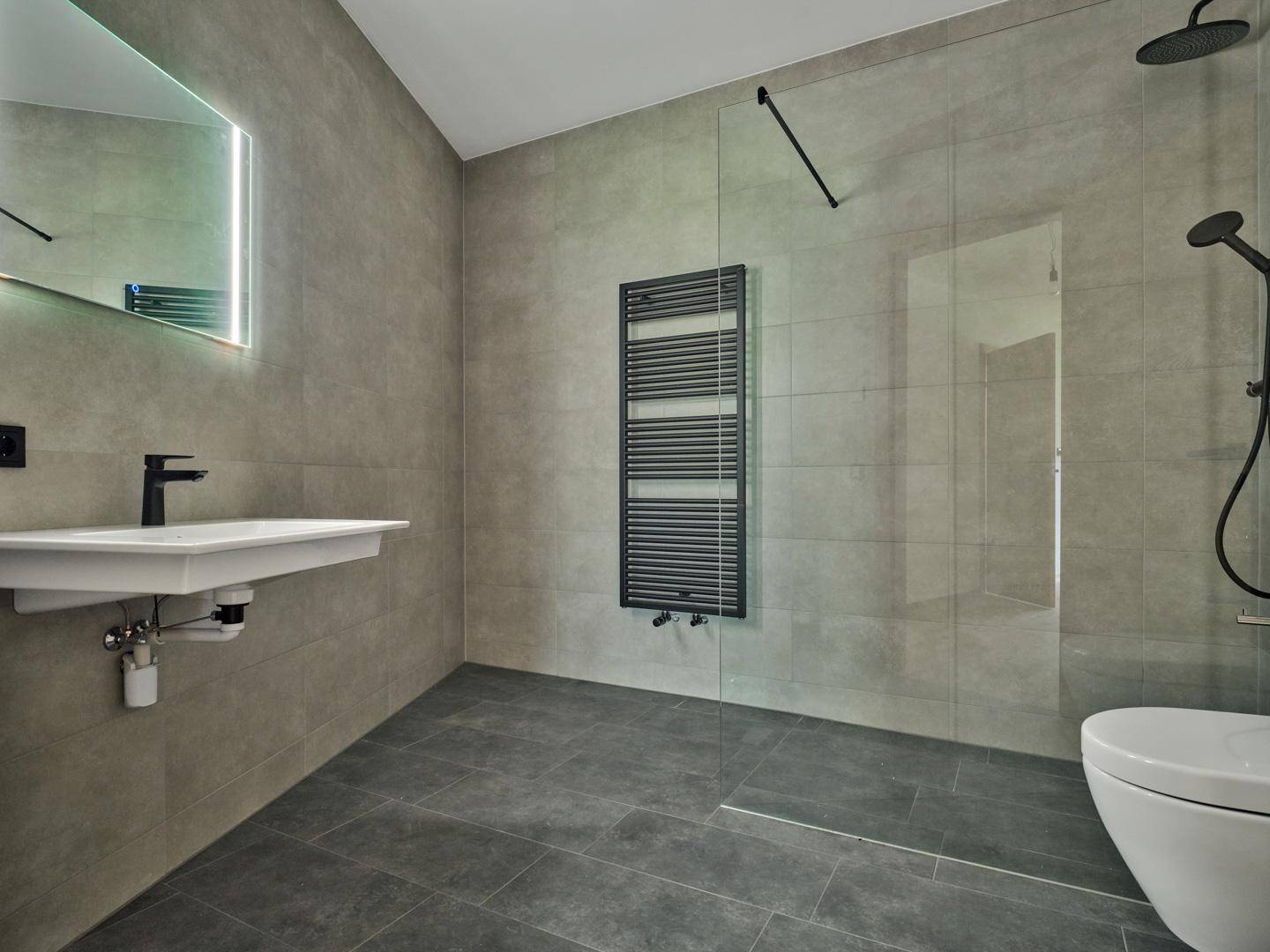 Modernes Badezimmer mit grauen Fliesen, ebenerdiger Dusche und beheiztem Handtuchhalter.