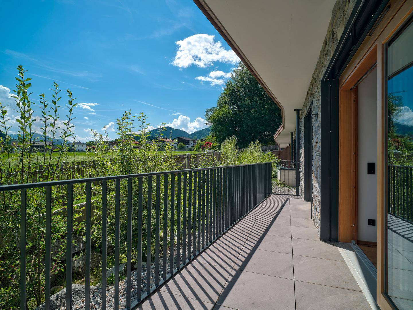 Langer Balkon mit Fliesenboden und Metallgeländer, bietet einen weiten Blick auf die grüne Landschaft und Berge.