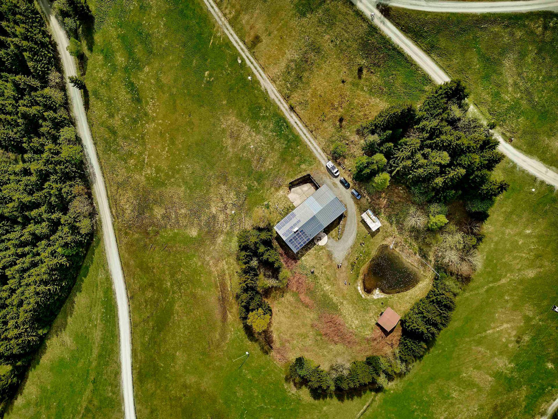Luftaufnahme des Anwesens mit Haus, Teich und Photovoltaikanlage auf dem Dach.