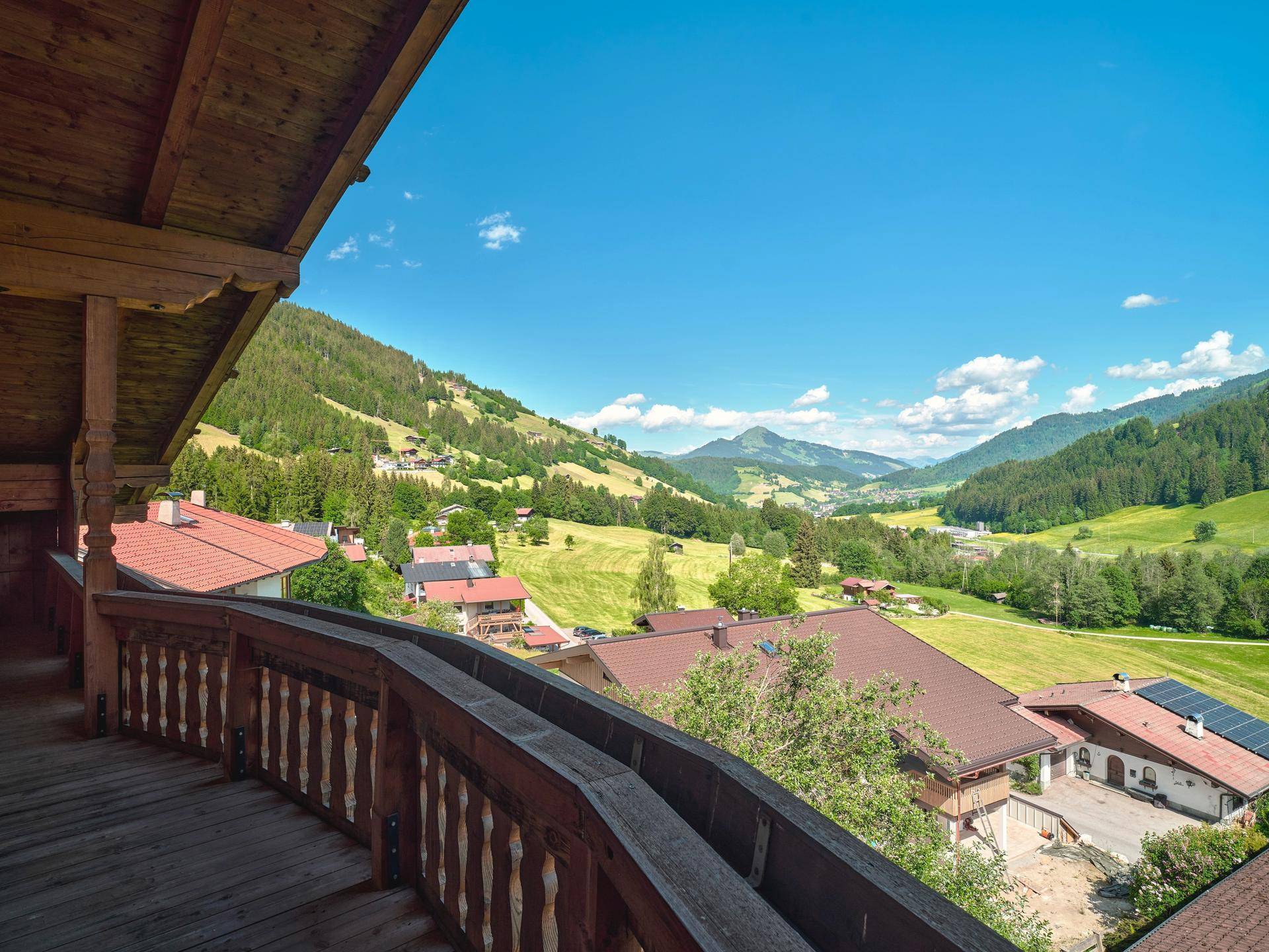 Blick von einem traditionellen Holzbalkon auf ein grünes Tal mit Häusern und Bergen.