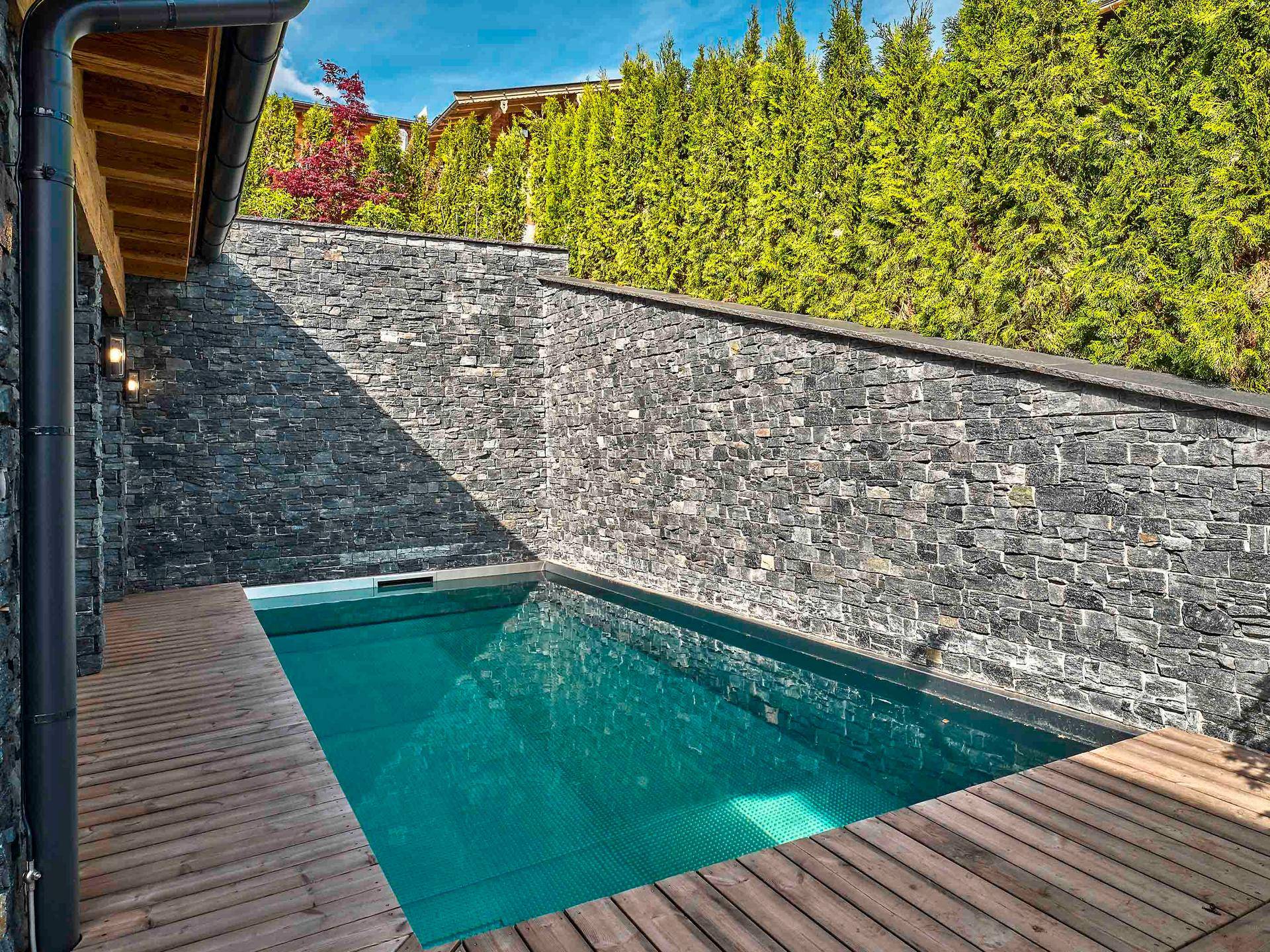 Kleiner Außenpool mit Holzdeck und Natursteinmauer, ideal zur Entspannung im Freien.