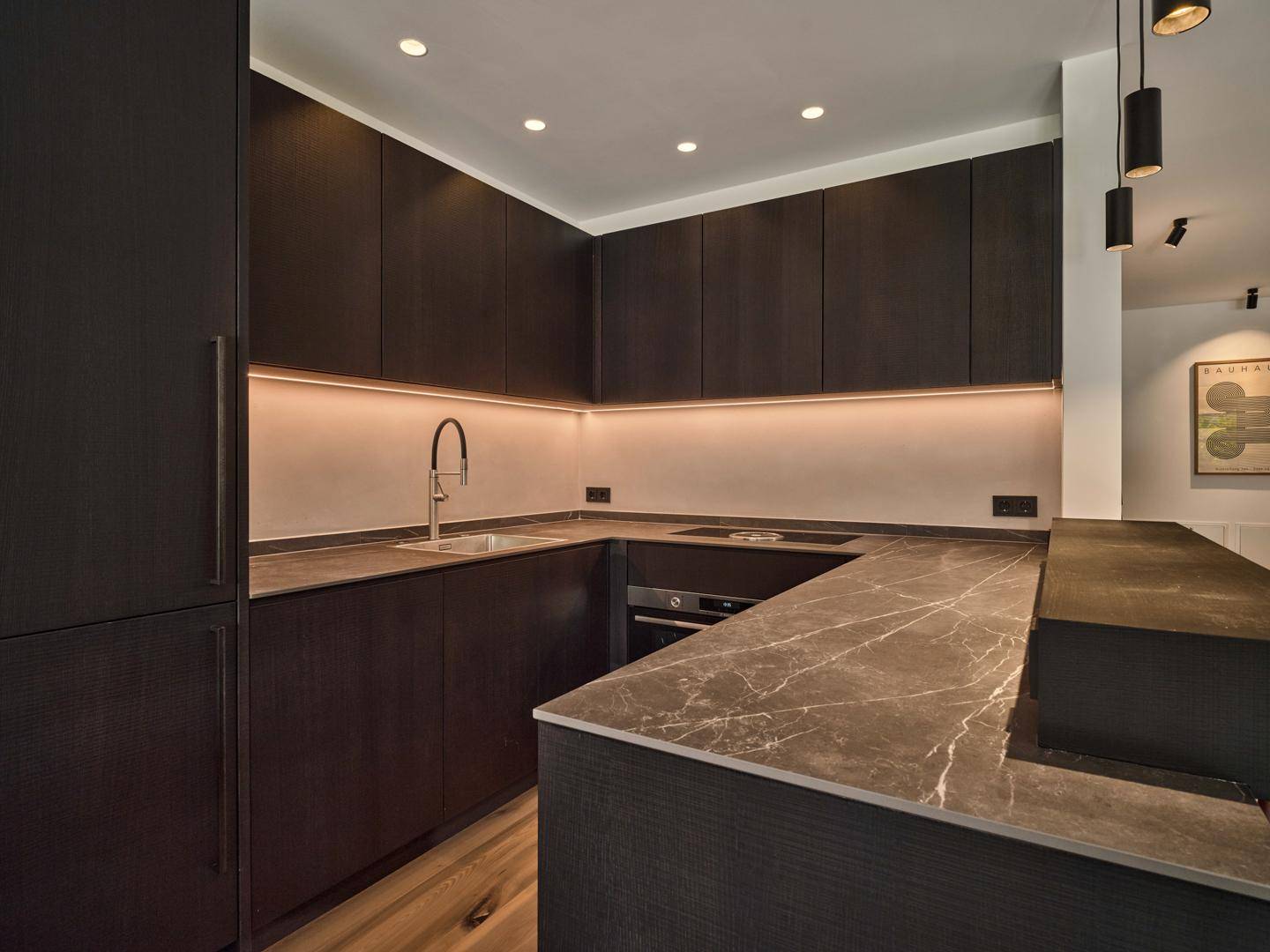 Moderne Küche mit dunklen Schränken, integrierten Geräten und einer eleganten Arbeitsplatte in Marmoroptik.