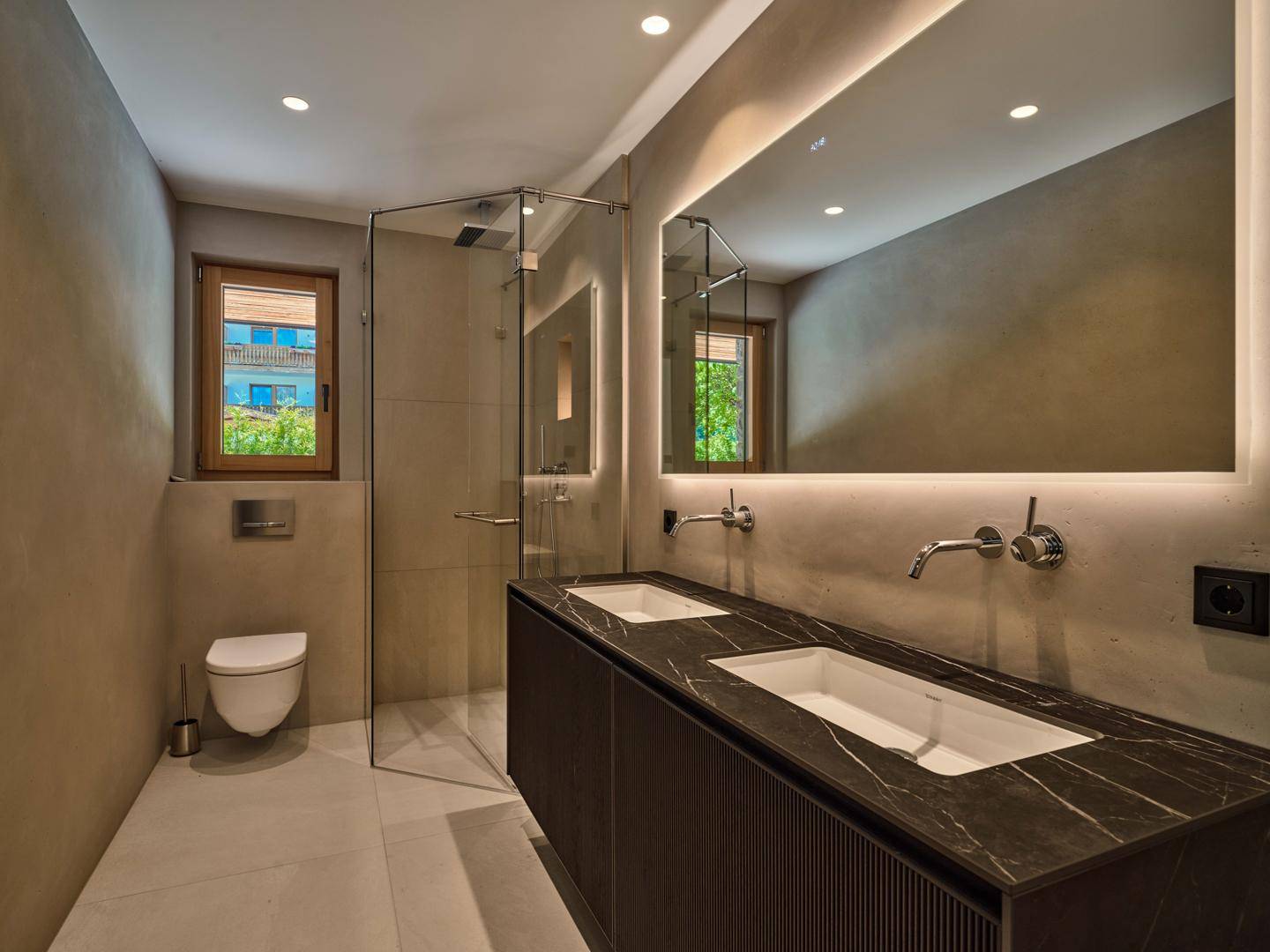 Modernes Badezimmer mit Doppelwaschbecken, begehbarer Dusche, beleuchtetem Spiegel und einem Fenster für Tageslicht.