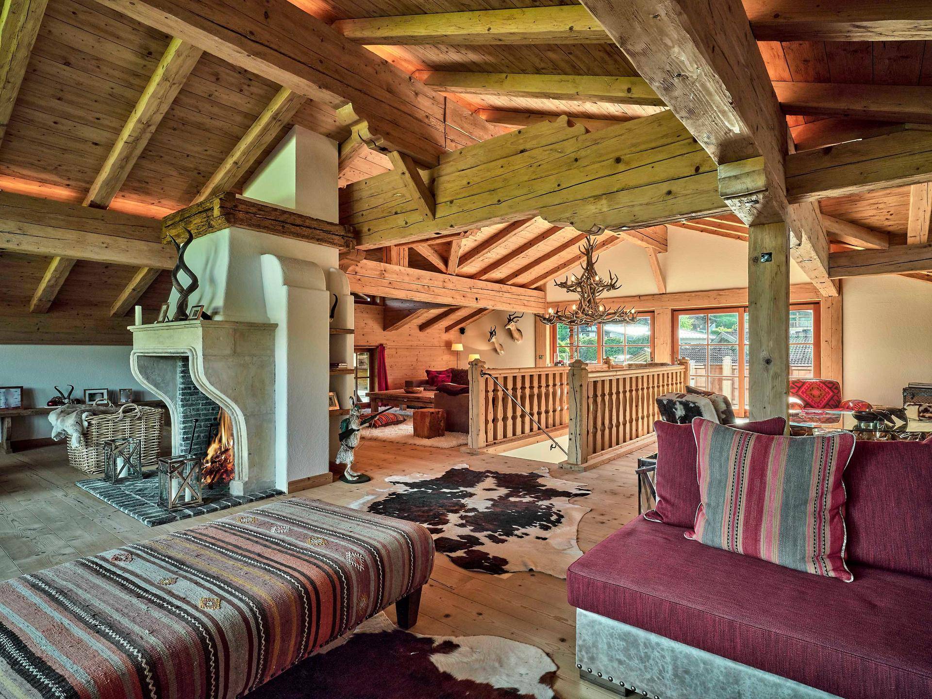 Geräumiges Wohnzimmer im alpinen Stil mit offenem Kamin, sichtbaren Holzbalken und hohen Decken.