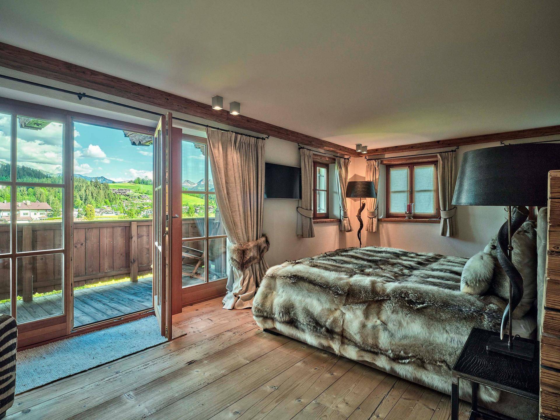 Helles Schlafzimmer mit Holzboden, Balkonzugang und weitem Blick auf die umliegende Berglandschaft.