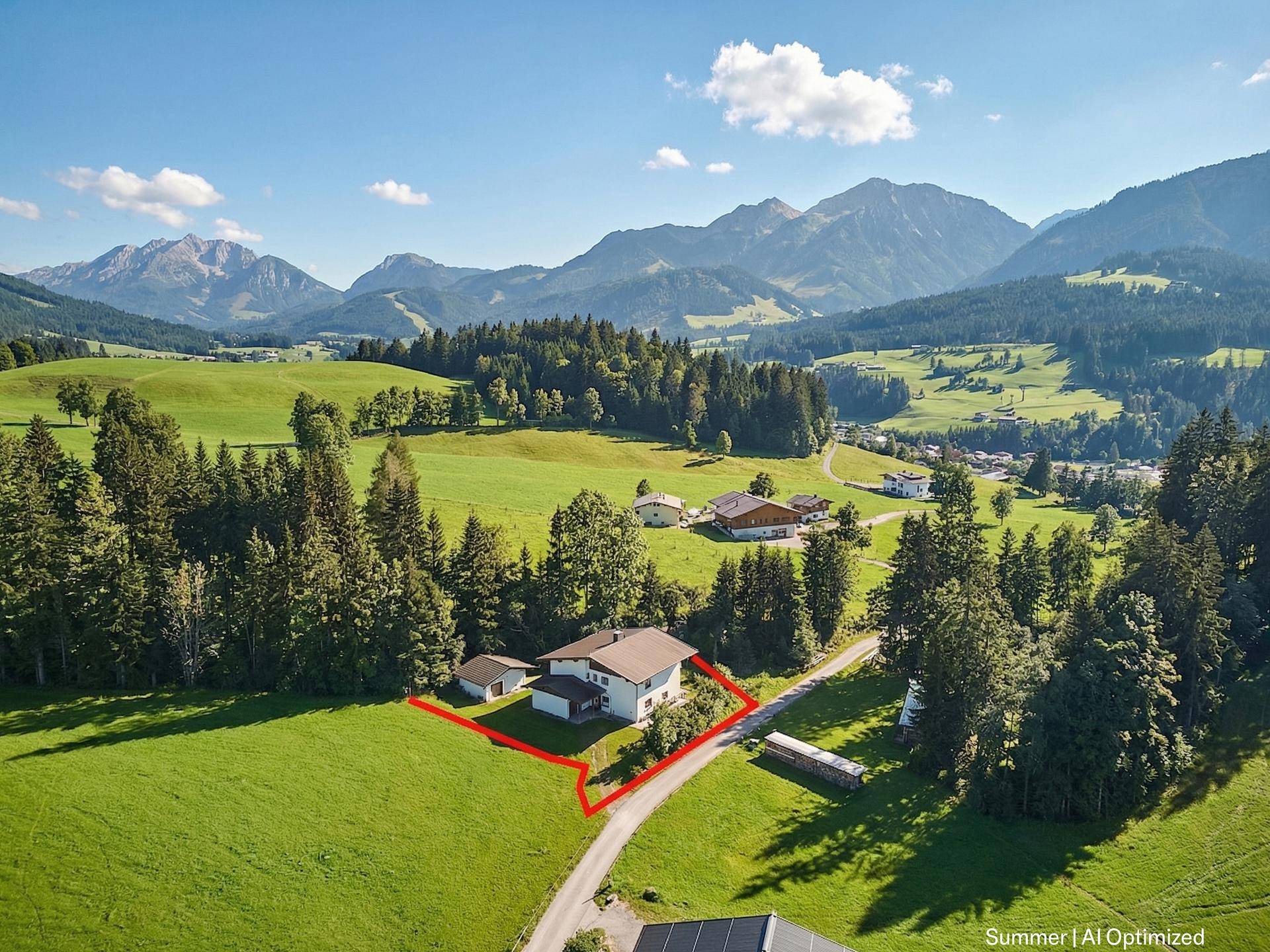 Luftaufnahme eines Hauses mit Grundstücksgrenze in einer malerischen Berglandschaft bei Sonnenschein.