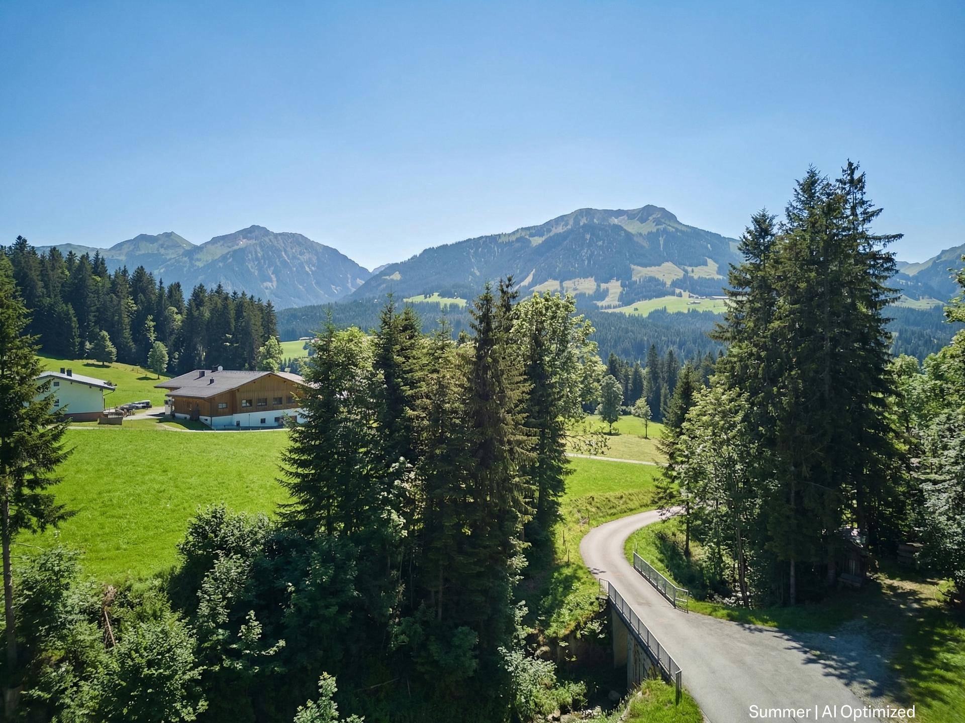 Serpentinenstraße mit Brücke und weitem Blick auf die umliegende Berglandschaft und ein Haus.