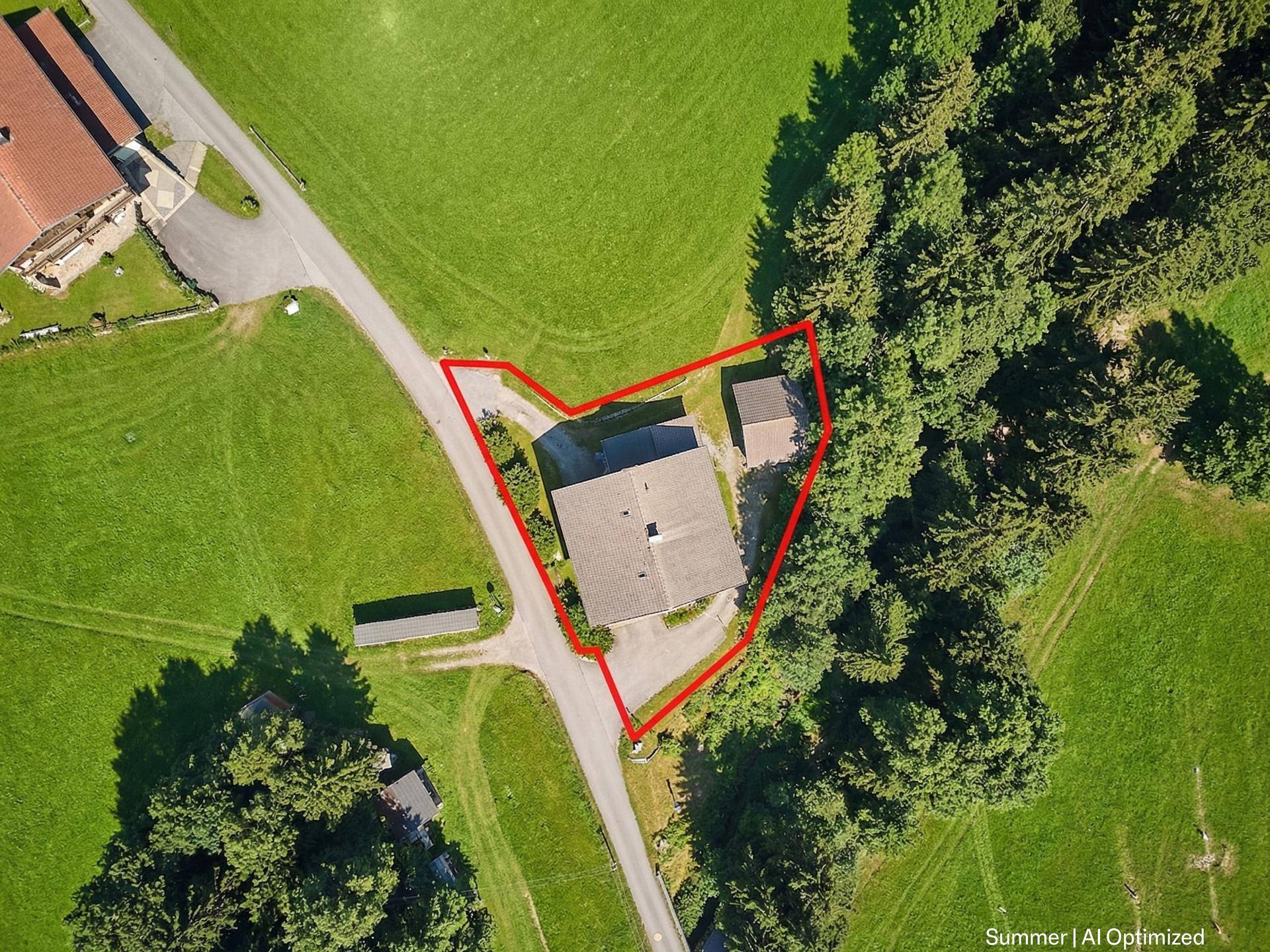 Vogelperspektive eines Hauses mit Grundstücksgrenze, umgeben von Wiesen und Wald.
