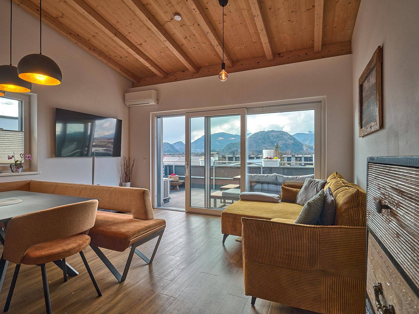 Gemütliches Wohnzimmer mit Holzbalkendecke, Zugang zur Terrasse und Bergblick.