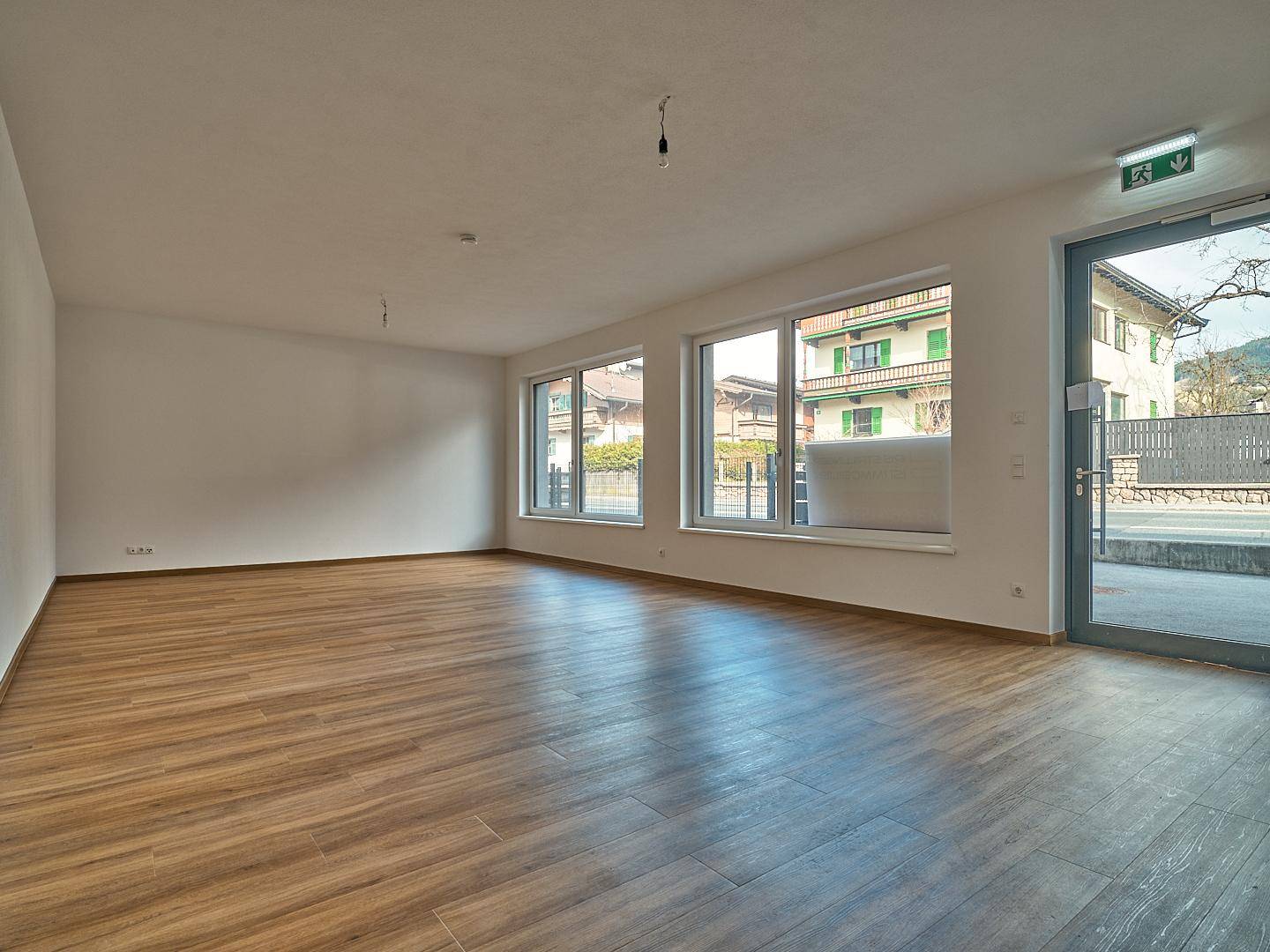 Geräumiger, unmöblierter Raum mit großen Fenstern und hellem Laminatboden.