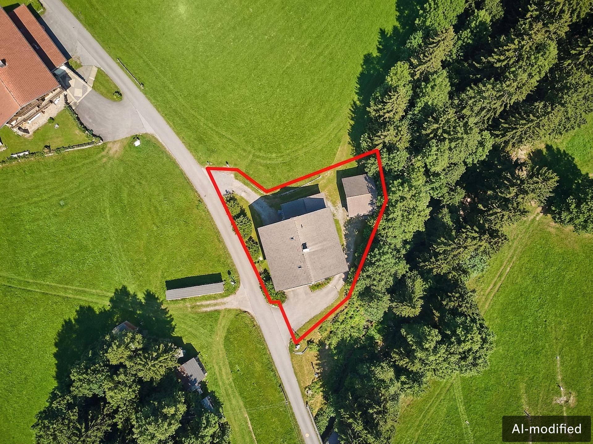 Draufsicht auf das Grundstück mit Haus und Nebengebäude, umgeben von grünen Wiesen und Wald.