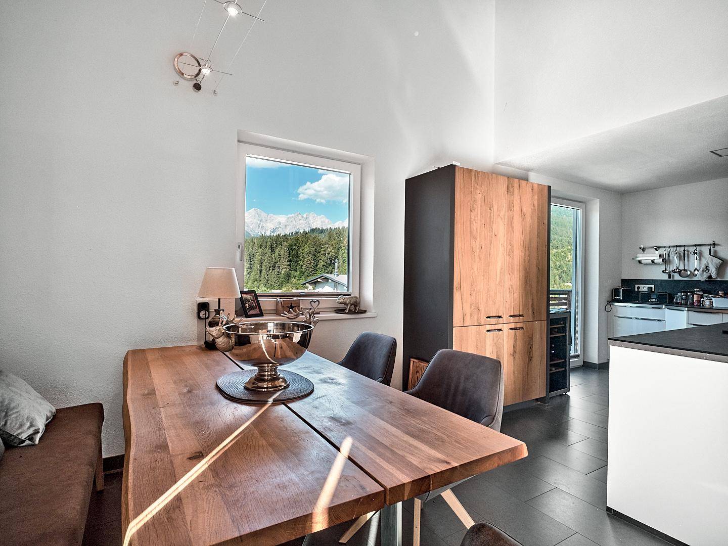 Heller Essbereich mit rustikalem Holztisch, modernen Stühlen und Fensterblick auf die Berge.