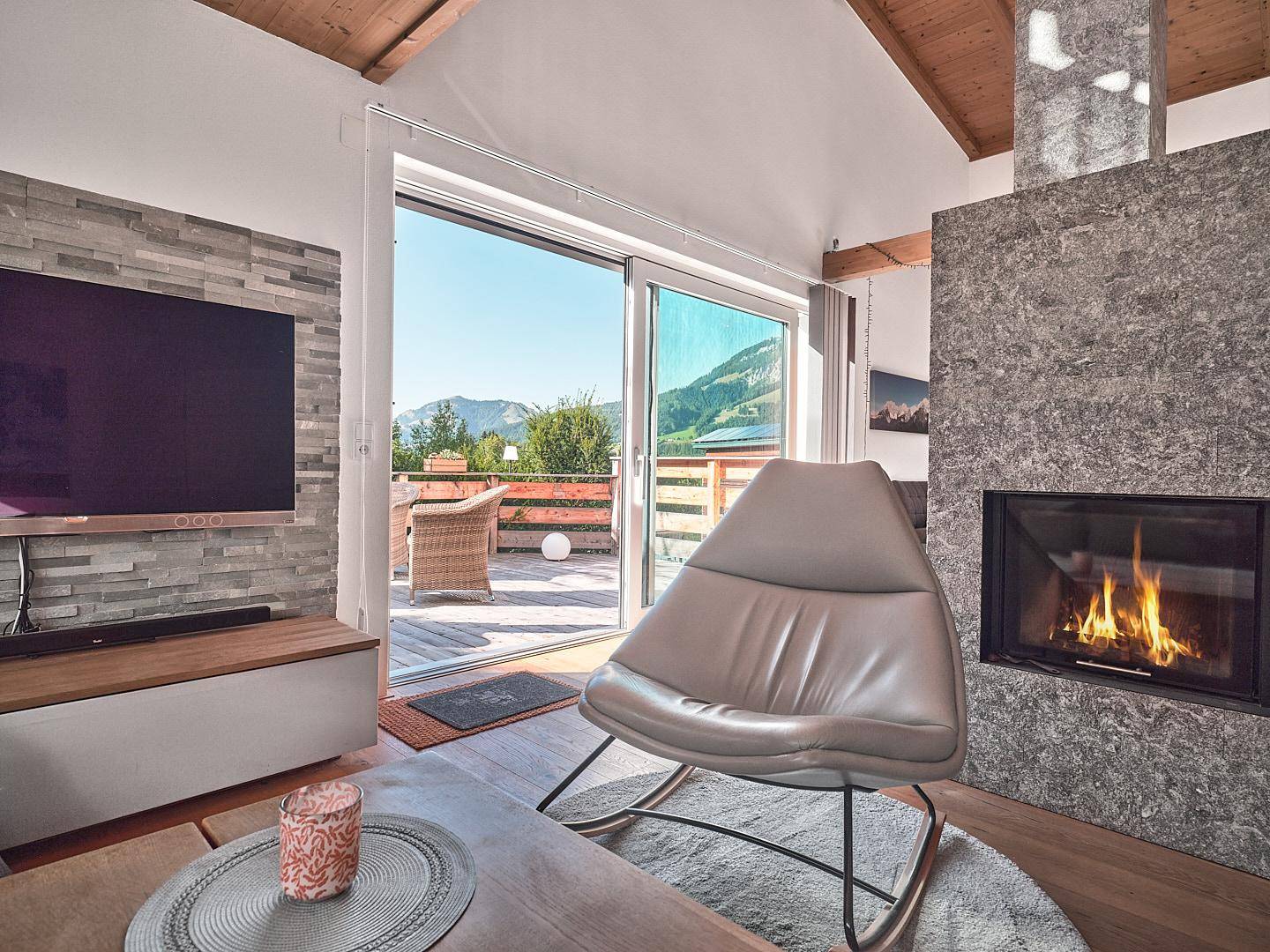 Gemütliches Wohnzimmer mit modernem Kamin, Holzbalkendecke und Zugang zur Terrasse mit Bergblick.
