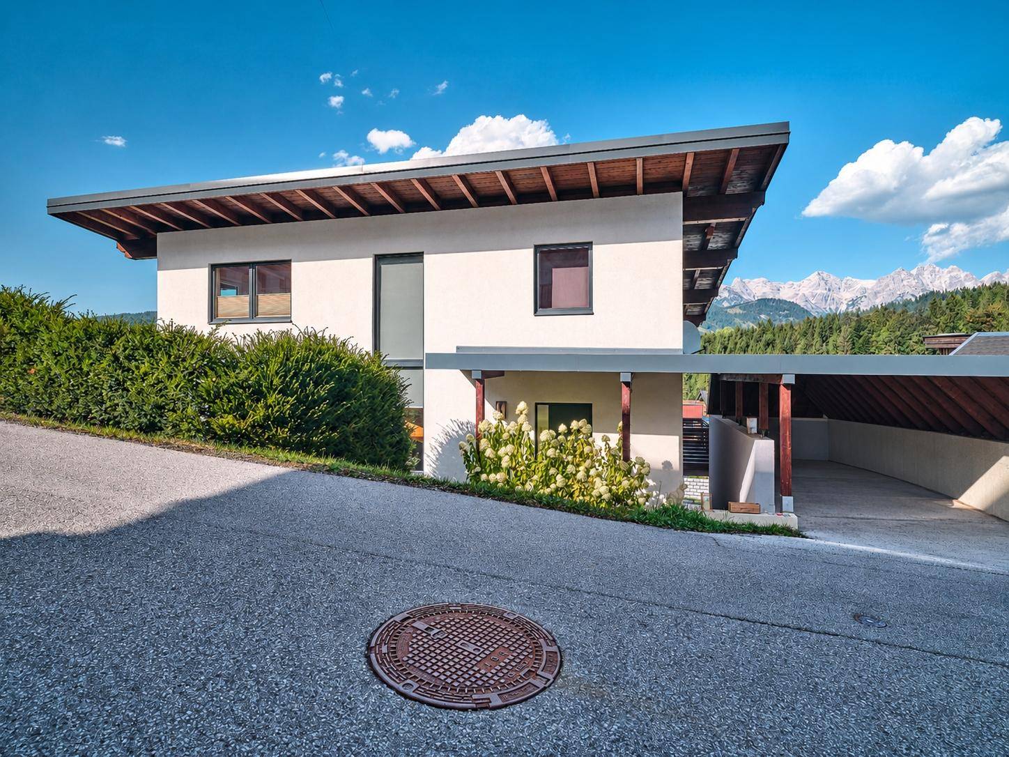 Modernes Einfamilienhaus mit Flachdach, Carport und Bergblick in einer grünen Umgebung.