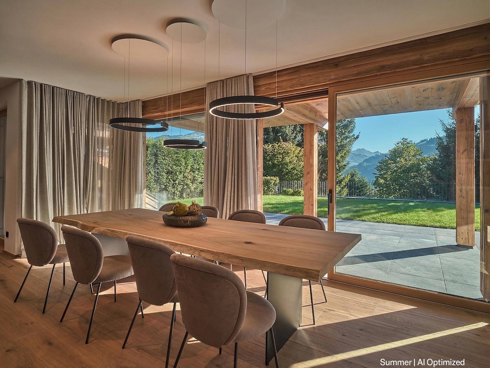 Eleganter Essbereich mit großem Holztisch, modernen Leuchten und Panoramablick auf die Berge.