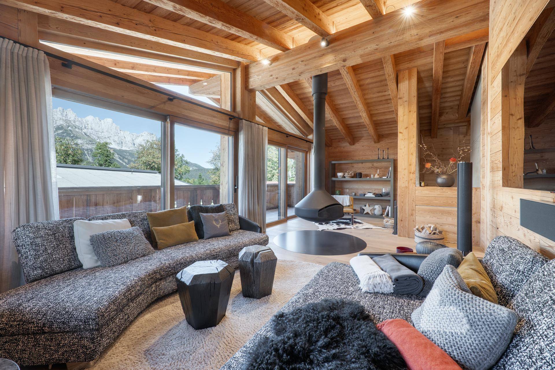 Gemütliches Wohnzimmer mit Holzelementen, Kamin und Panoramafenstern mit Bergblick.