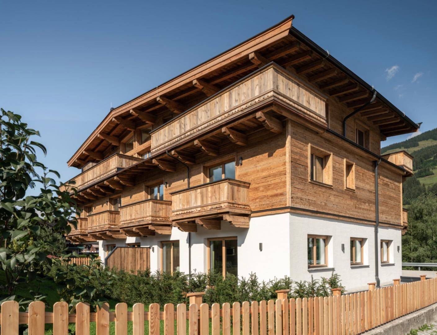 Traditionelles Holzhaus im alpinen Stil mit mehreren Balkonen und gepflegtem Vorgarten.