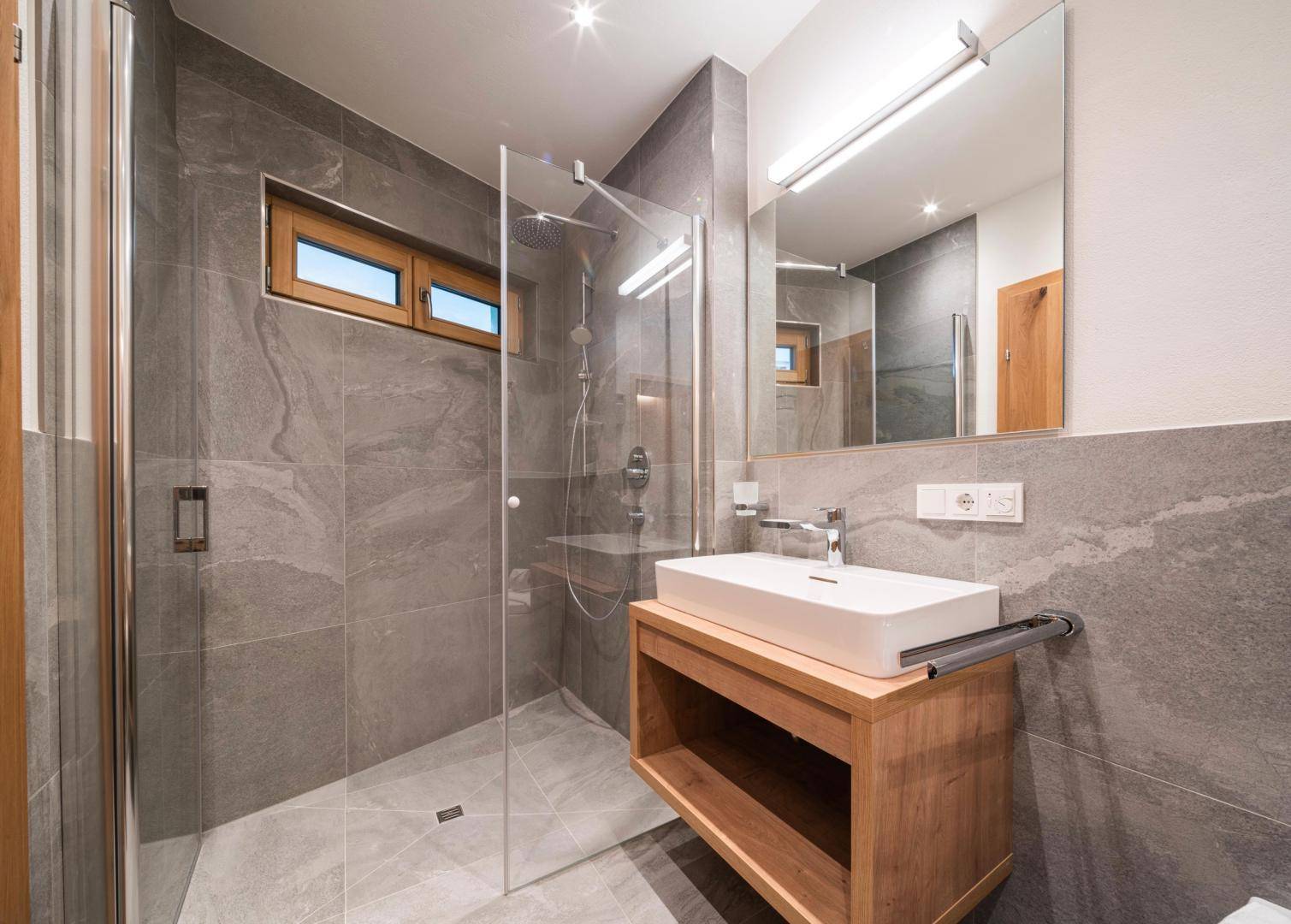 Modernes Badezimmer mit begehbarer Dusche, Einzelwaschbecken und großformatigen grauen Fliesen.