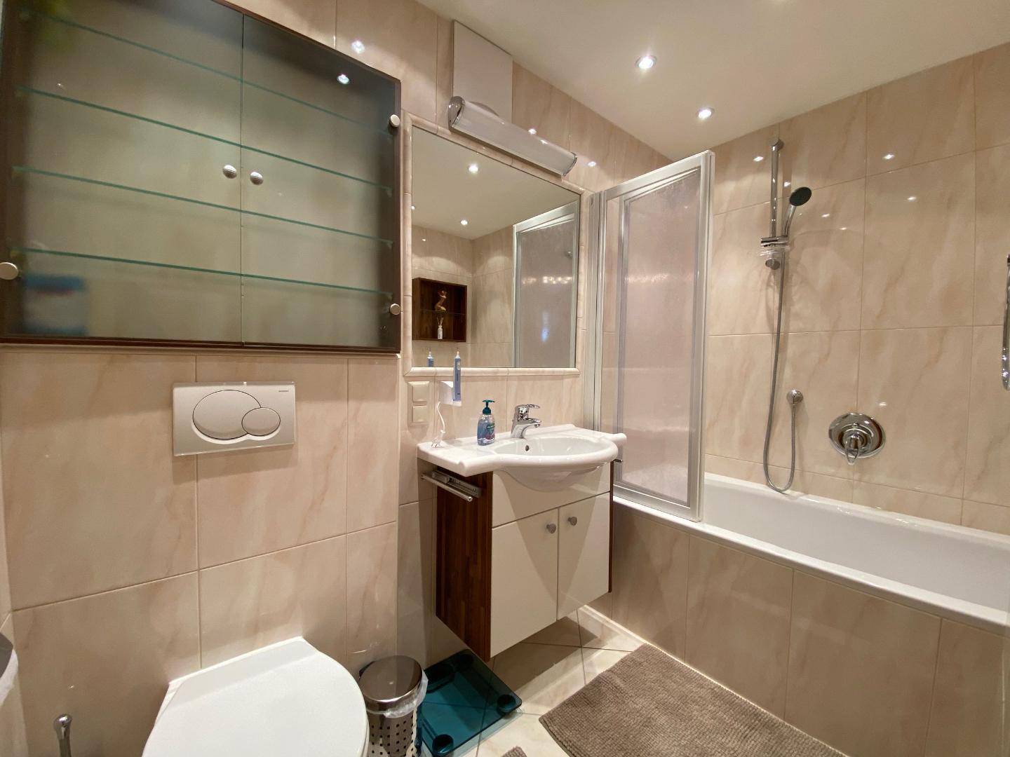Gefliestes Badezimmer mit Badewanne, Duschfunktion und integriertem WC.