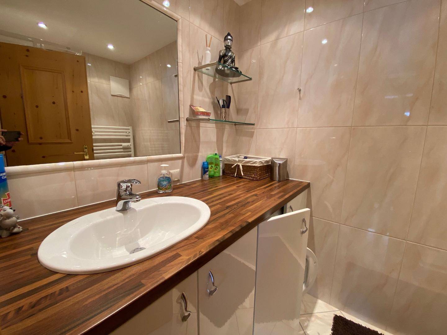 Modernes Badezimmer mit Holzwaschtisch, ovalem Waschbecken und hellen Fliesen.