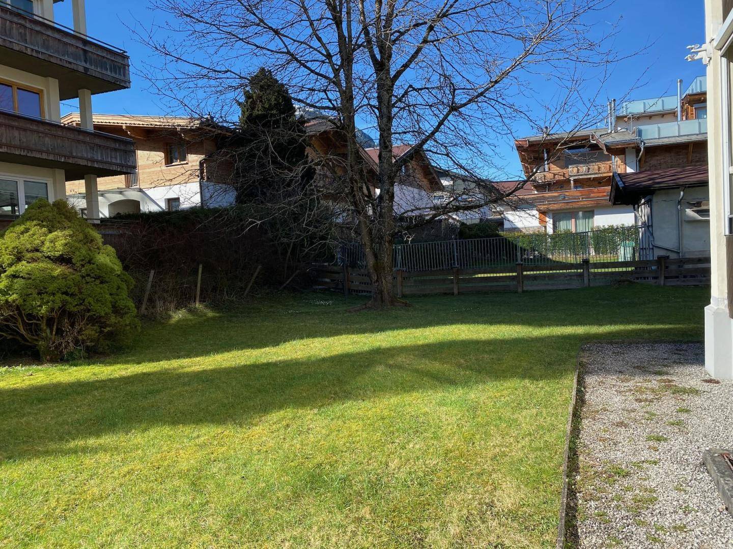 Gepflegter Rasenbereich des Gartens mit Bäumen und Blick auf die umliegenden Häuser.