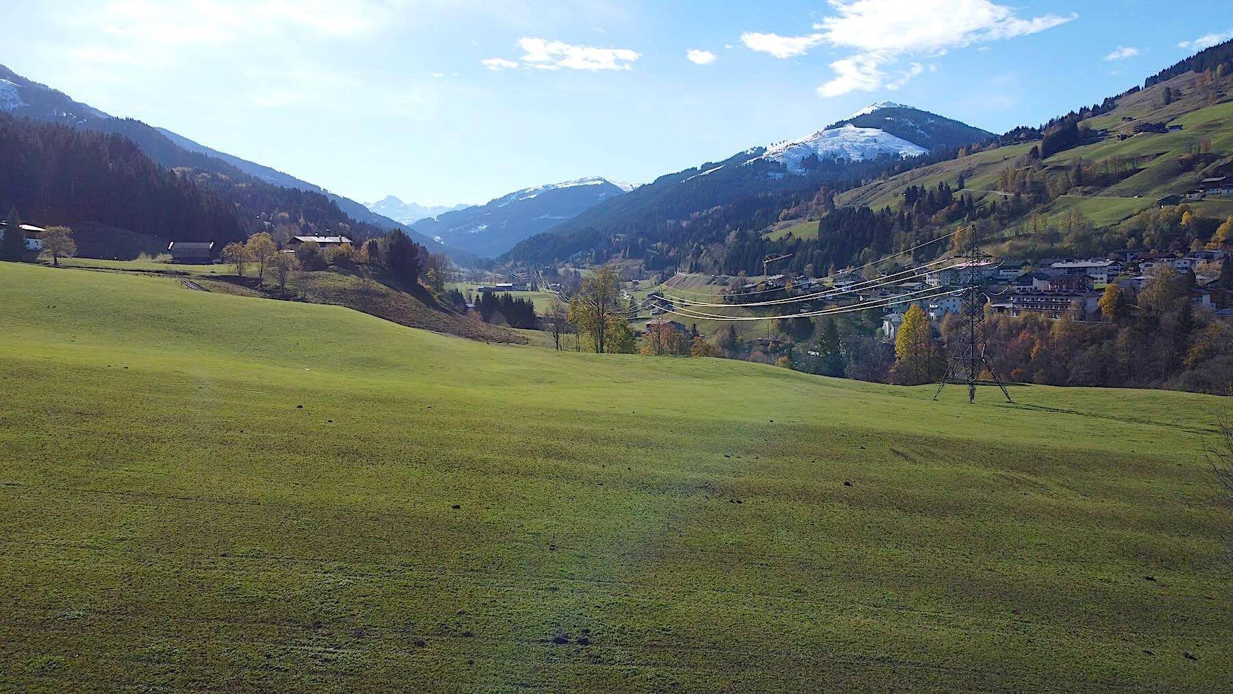 Panoramablick über eine weite grüne Landschaft mit Bergen, teilweise schneebedeckt, und einem sonnigen Himmel.