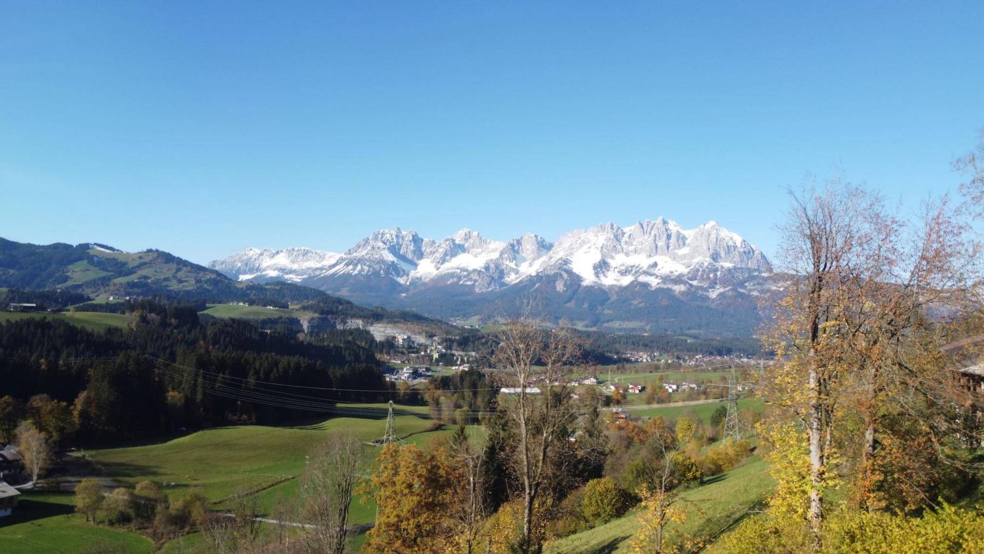Panoramablick auf schneebedeckte Berge und grüne Täler unter einem klaren blauen Himmel.