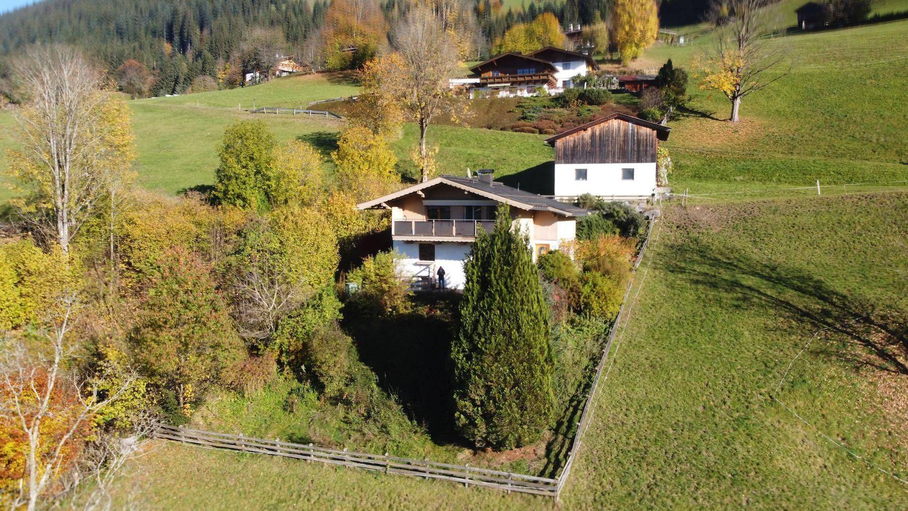 Luftaufnahme eines Hauses in Hanglage, umgeben von herbstlicher Vegetation und grünen Wiesen.