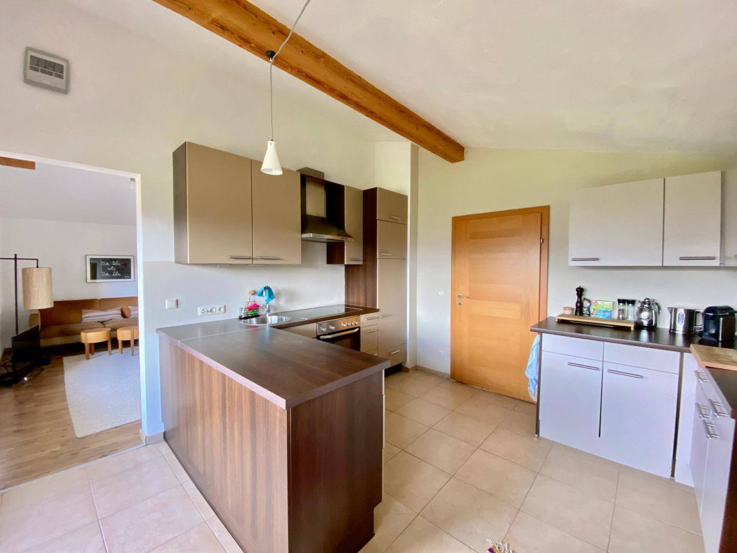 Funktionale Küche mit hellbraunen Schränken, Fliesenboden und einer Holztheke, offen zum Wohnbereich.